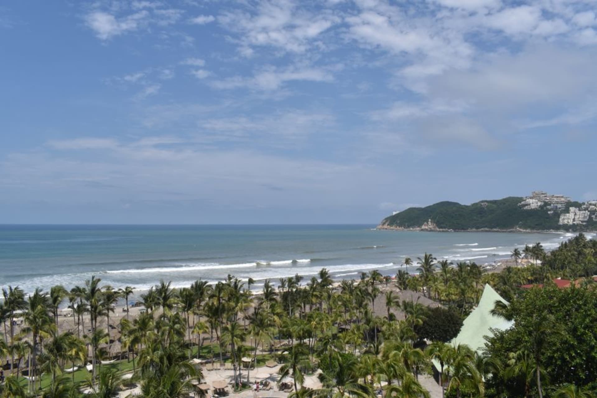 Wide sandy beach at Playa del Palmar in Ixtapa with palm trees, resort hotels in the distance, and calm Pacific surf at low tide 