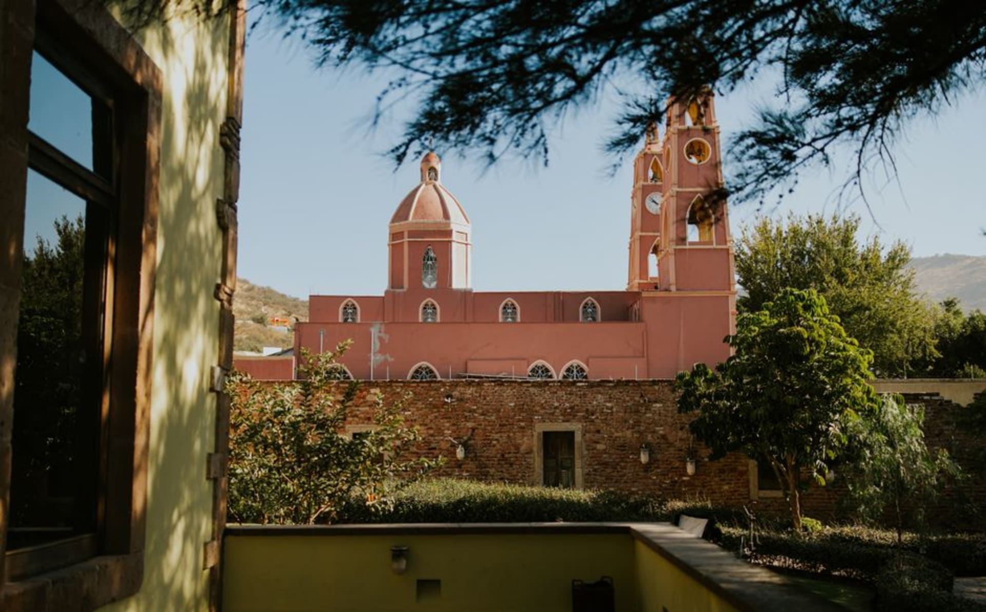 The baroque facade of Linares cathedral glowing in late-afternoon light, flanked by palm trees and a quiet plaza