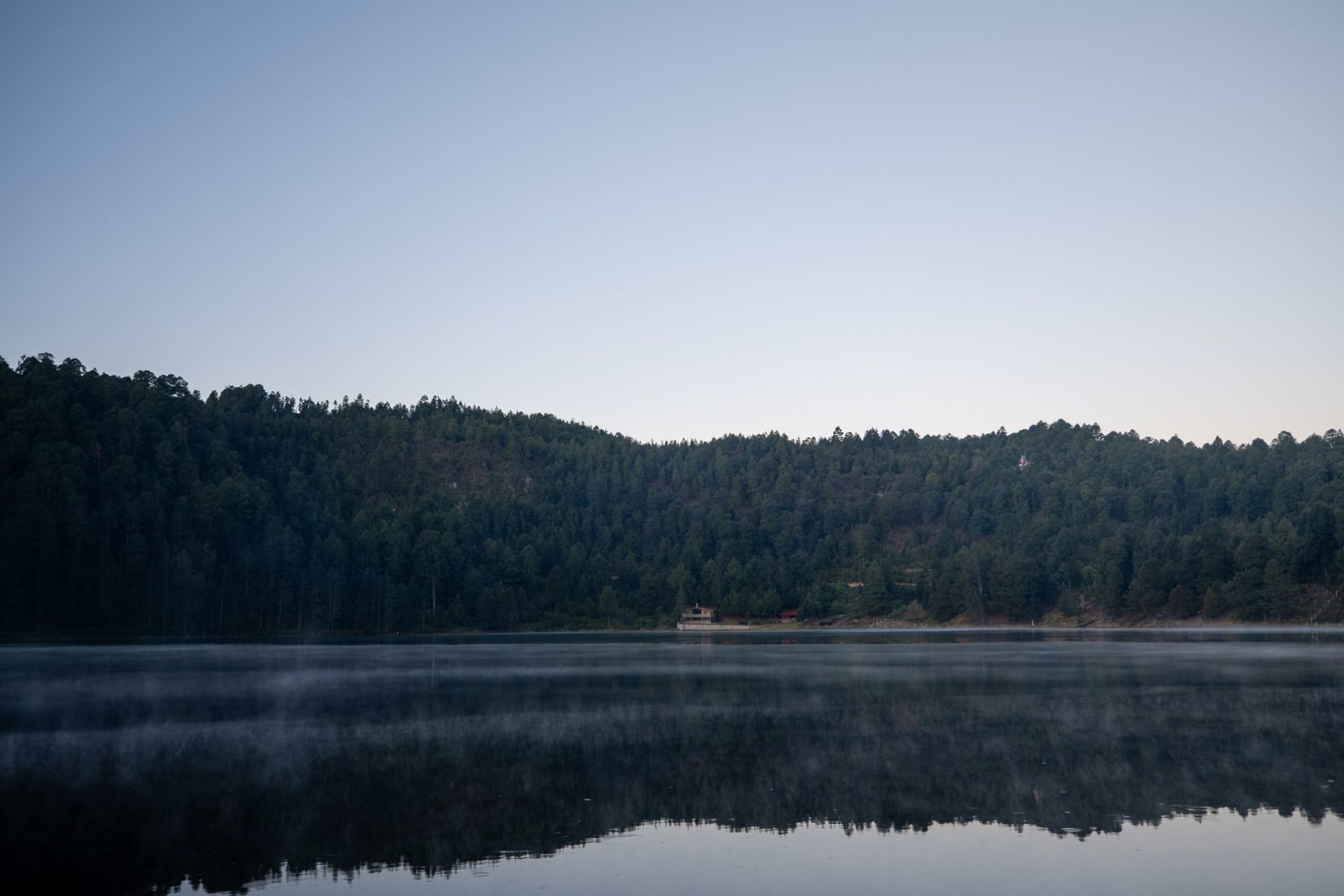 Lago de Tejamaniles at Los Azufres, the green geothermal water in a forested basin with pine and oyamel fir on the surrounding slopes, steam rising from a fumarole near the far shore