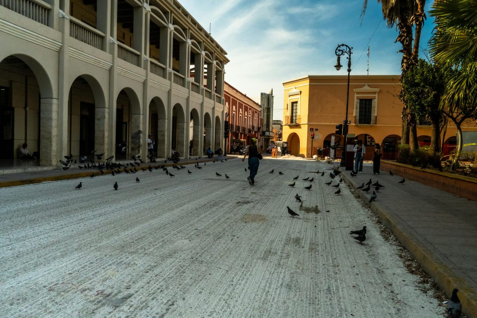 A sun-bleached colonial plaza in Merida, Yucatan, with pale limestone facades, ornate cathedral towers, and bougainvillea spilling over wrought-iron balconies in the late morning light.