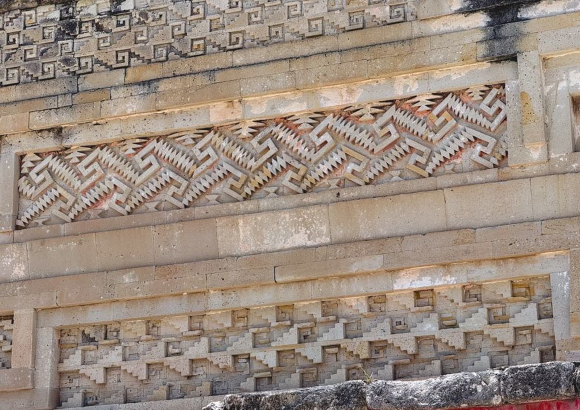 The intricate geometric stone mosaic panels at Mitla's Hall of Columns, the Zapotec fretwork patterns of interlocking stepped frets covering the interior walls in precise carved limestone, afternoon light