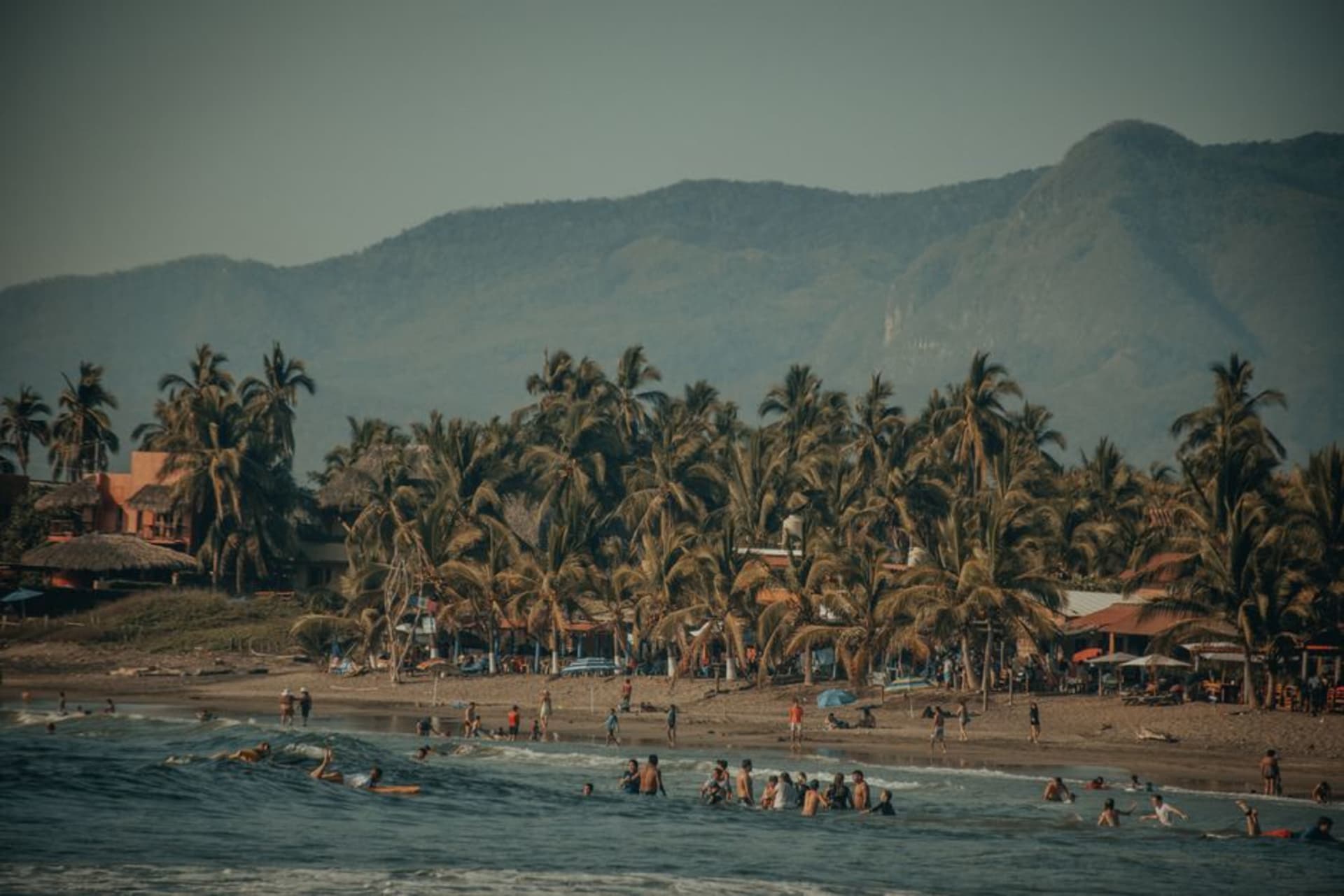 Black volcanic sand beach at Playa Ventura with fishing pangas pulled up near the waterline and coconut palms curving toward the Pacific