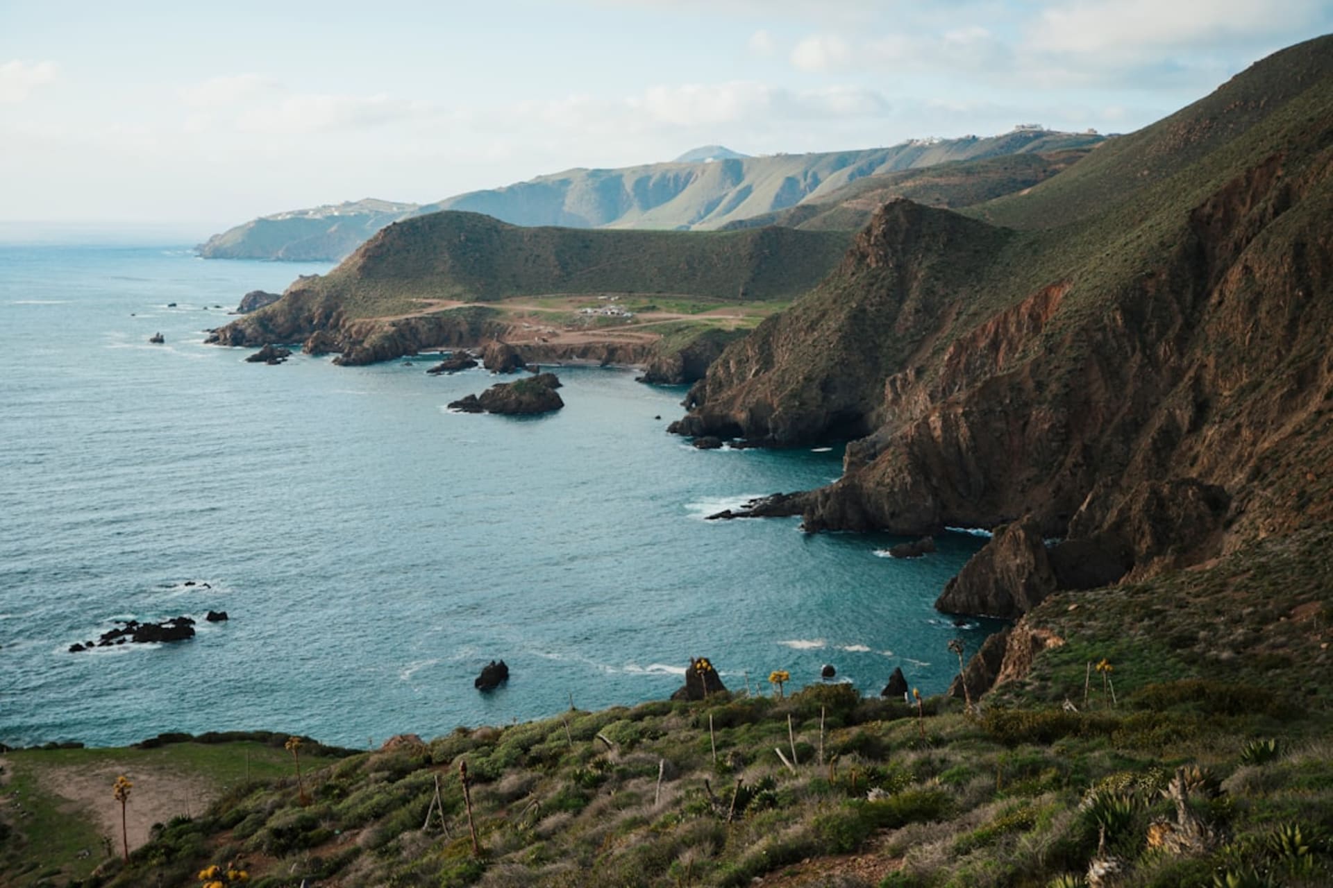 Wide Pacific horizon at Punta Abreojos, rocky point jutting into a grey-blue sea with low white fishing village buildings catching late afternoon light