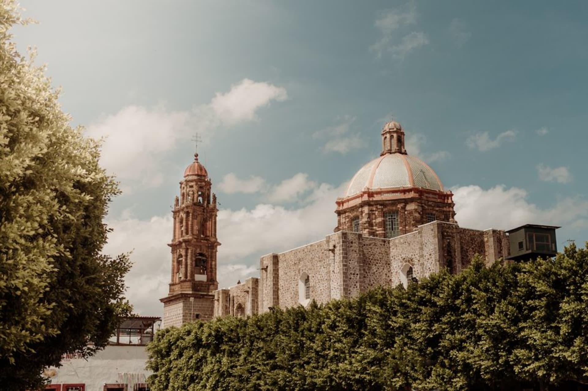 The Parroquia de San Francisco de Asís rising above the stone plaza, its rose-colored facade catching afternoon light against a pale blue sky
