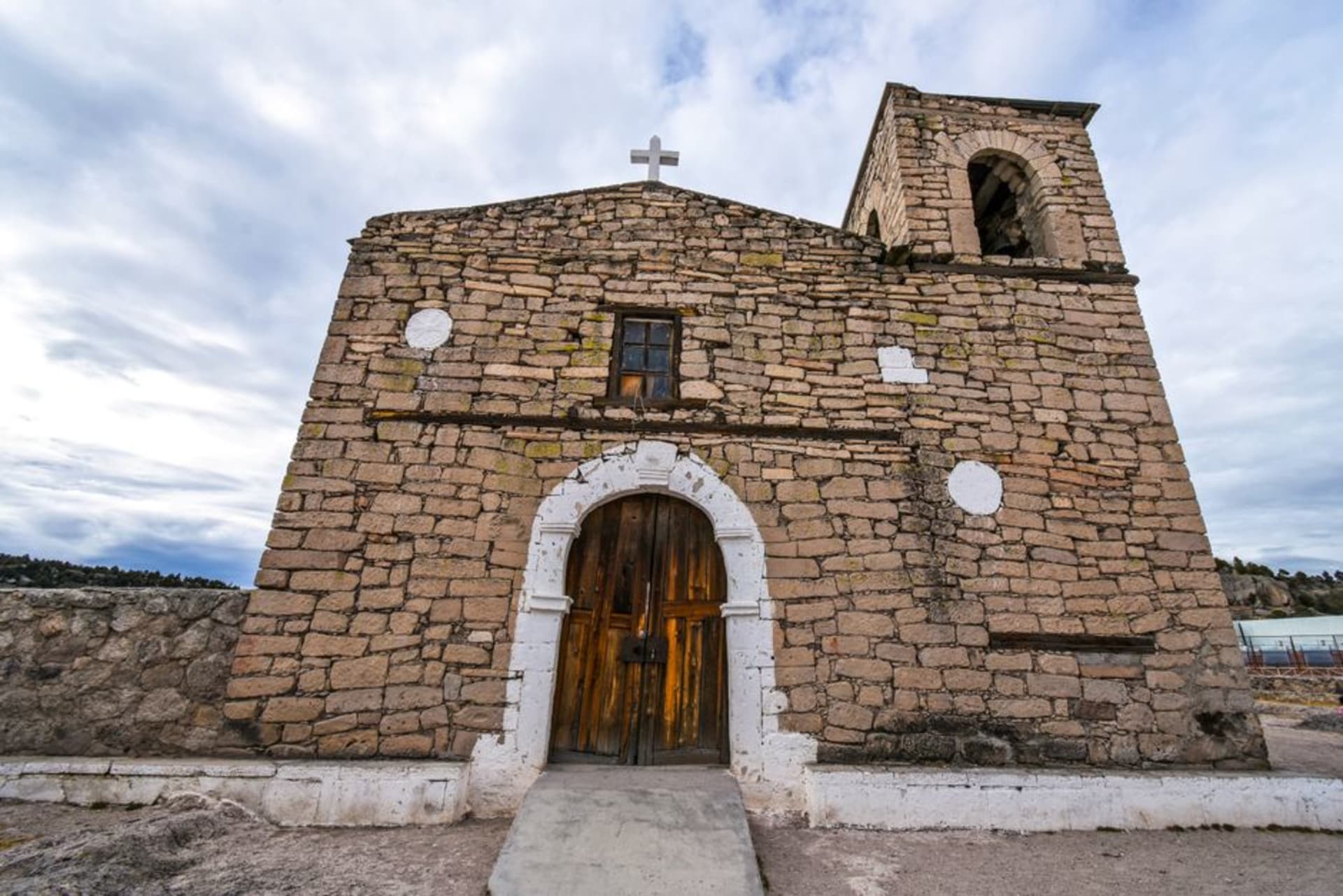 The baroque limestone facade of Misión San Francisco Javier rising above a dry sierra canyon, framed by ancient Jesuit-planted olive trees under a pale desert sky.