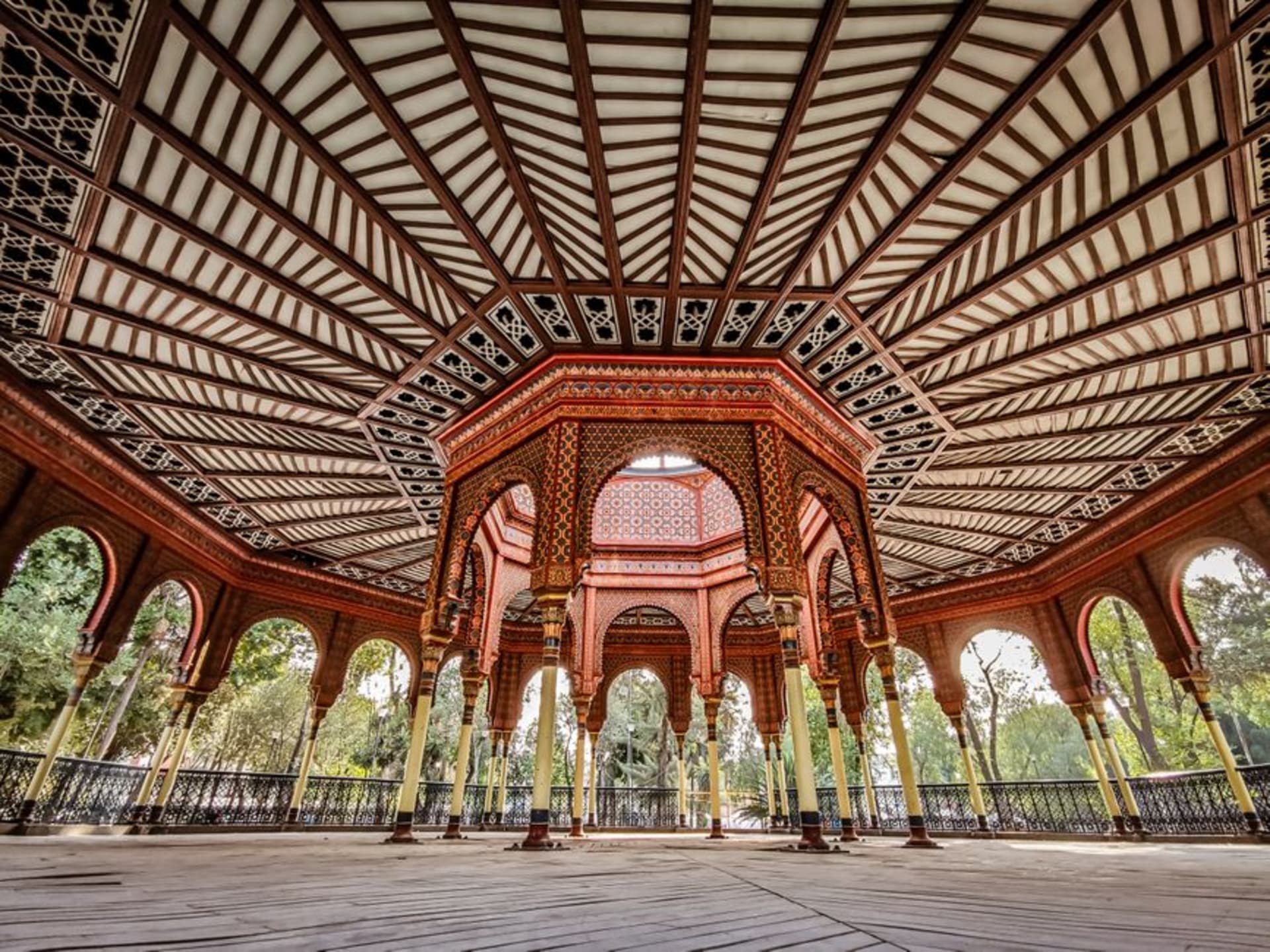 The Kiosco Morisco, an ornate Moorish cast-iron pavilion with blue and green tilework, rising above the tree-lined Alameda de Santa María in late afternoon light