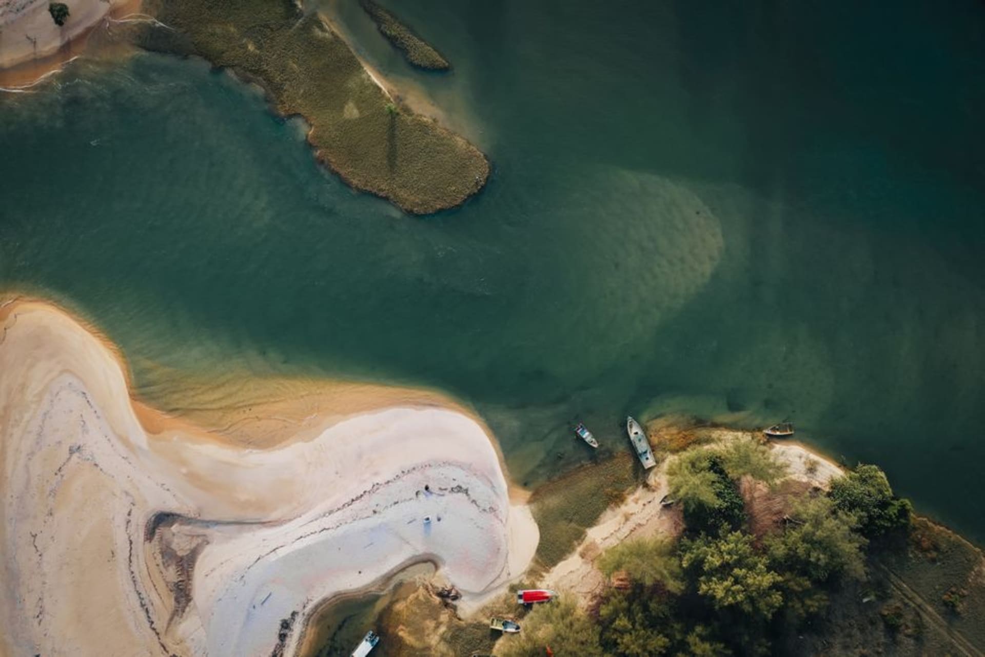 A narrow palm-lined peninsula with Pacific waves on one side and still mangrove waterways on the other, seen under the wide, low light of a Sinaloa afternoon.