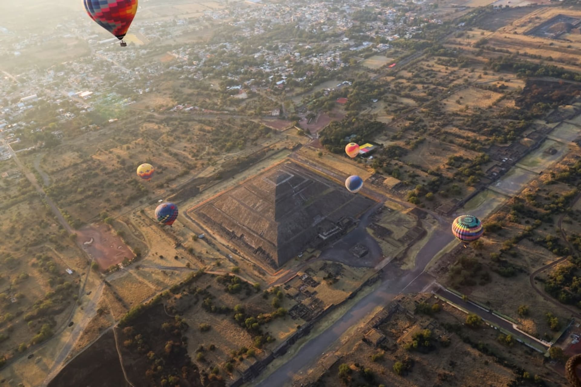 The Pyramid of the Sun at Teotihuacán at dawn, its massive stepped form rising from the Avenue of the Dead in golden early light, the city's grid stretching into the distance
