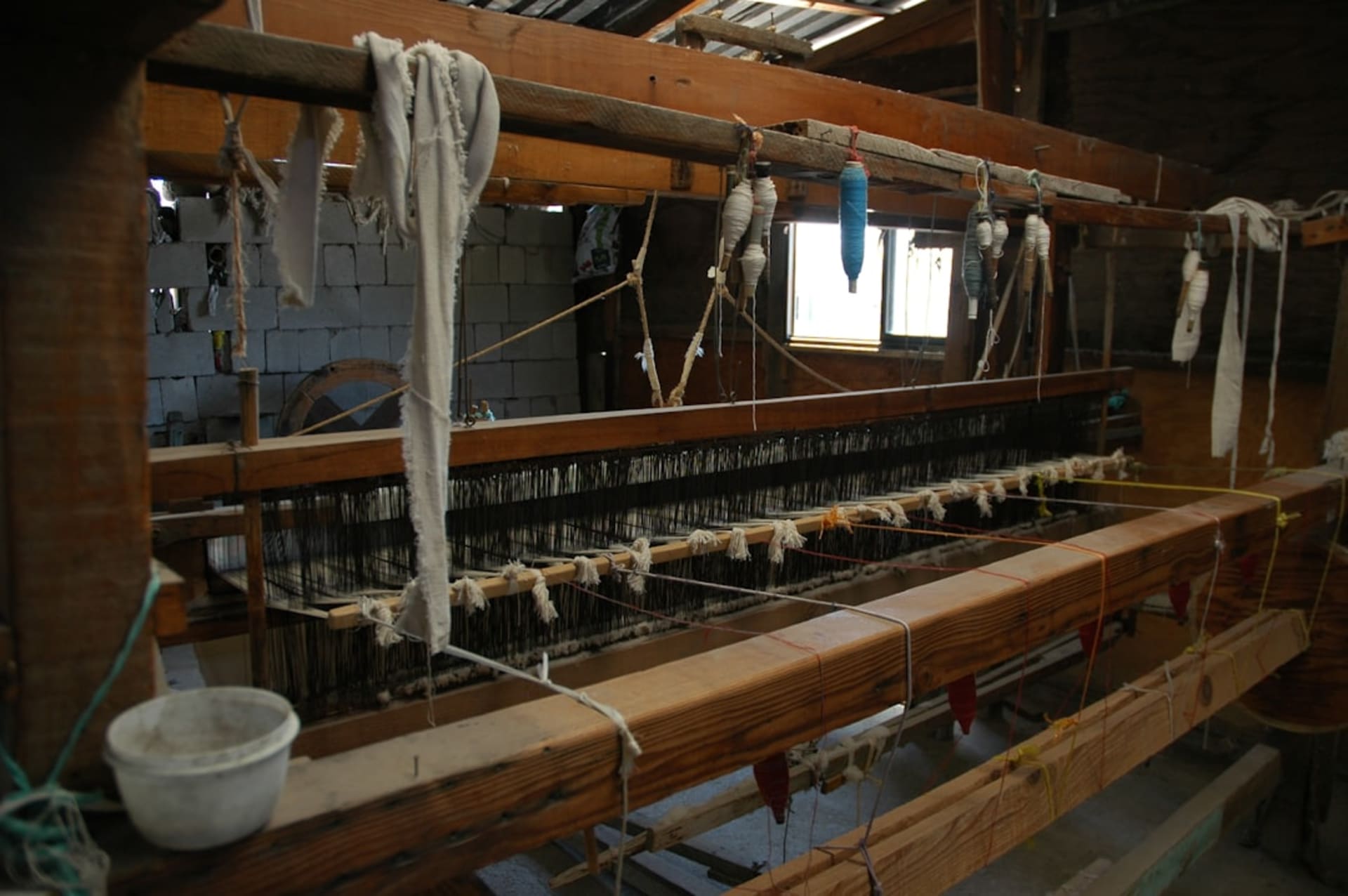A Zapotec weaver at a traditional backstrap loom in a Teotitlán del Valle workshop, working on a rug with geometric Zapotec patterns, skeins of cochineal-dyed wool in deep reds and purples hanging behind