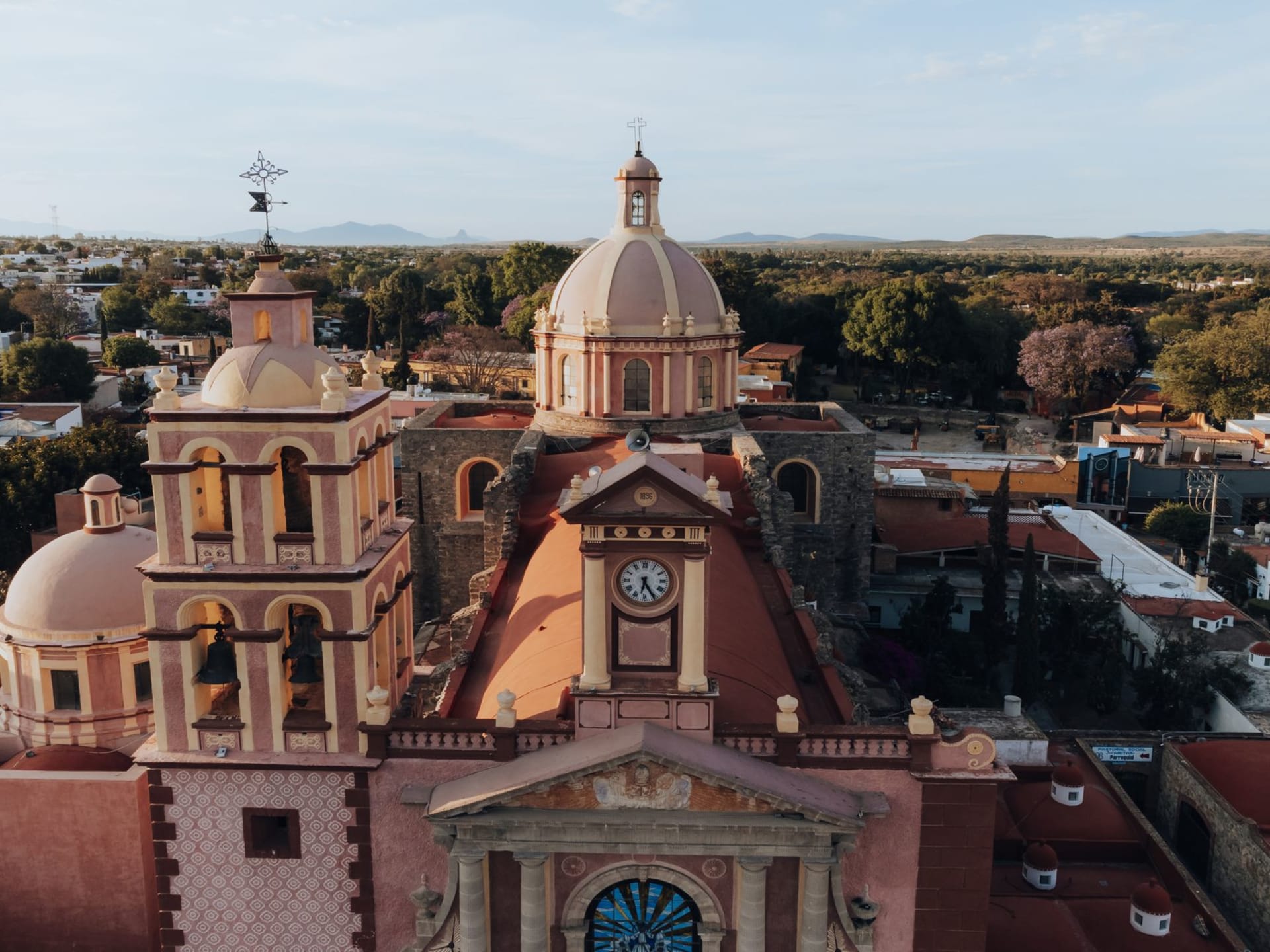 The main plaza of Tequisquiapan in late afternoon, pink quarry stone buildings and a colonial church with bougainvillea draped over a stone archway