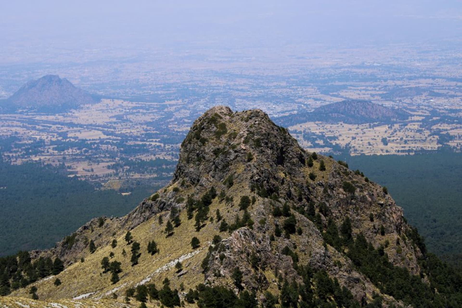 Pine-forested highlands around Terrenate in northeastern Tlaxcala, ridges of dark conifers under a cloudy sky, a dirt rancho road cutting through green pasture in the foreground