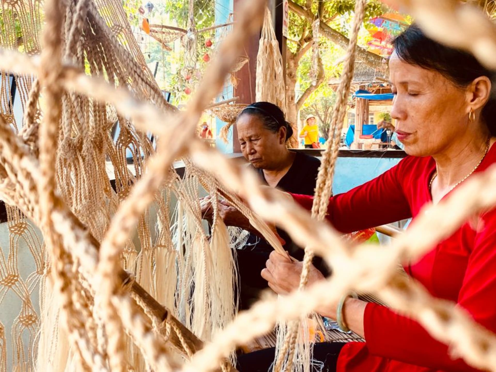 A woman weaves a cotton hammock in an open-air workshop in Tixkokob, warp threads stretching the full length of a sunlit room in earthy rust and white.