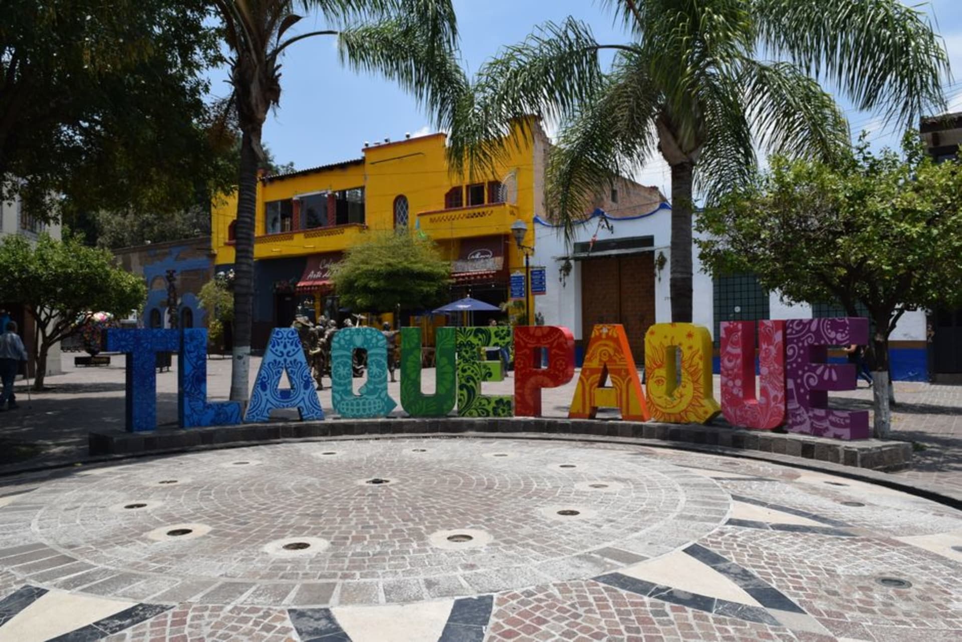 The pedestrian street of Independencia in Tlaquepaque lined with colonial buildings housing galleries and artisan workshops, bougainvillea cascading from wrought-iron balconies overhead