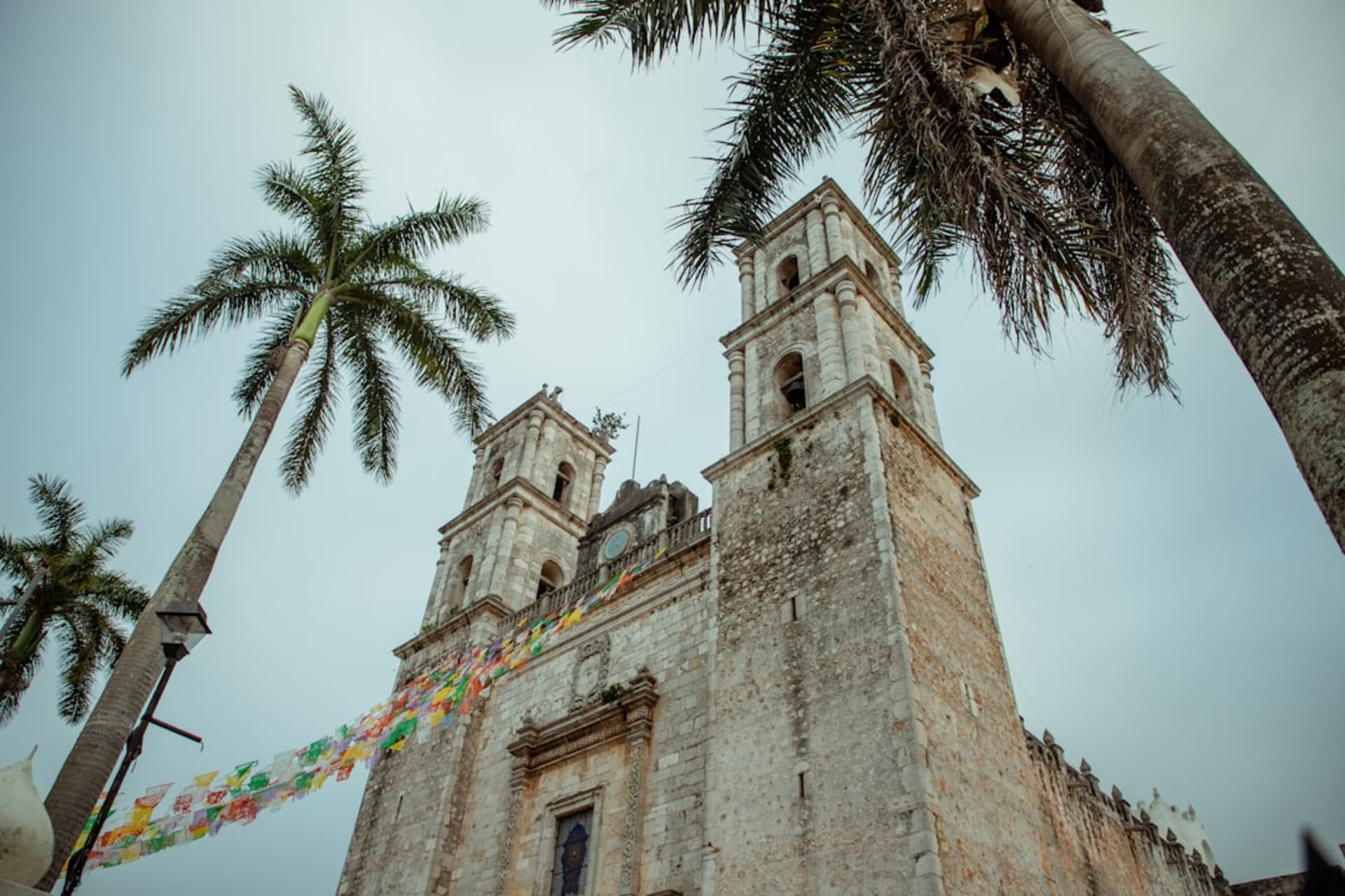 The pale yellow and white colonial church of San Servacio rising above Valladolid's Plaza Principal at dusk, palm trees silhouetted against the warm sky