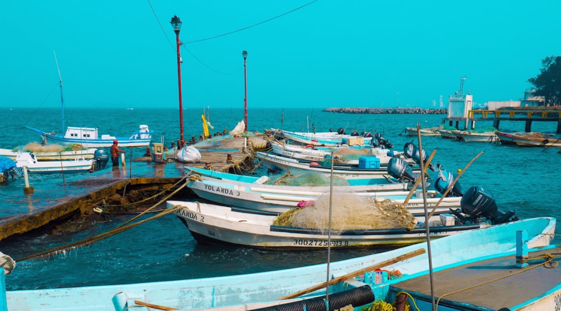 The colonial malecon of Veracruz at dusk with the fortress of San Juan de Ulúa visible across the harbor, fishing boats in the foreground and the Gulf of Mexico catching the last light
