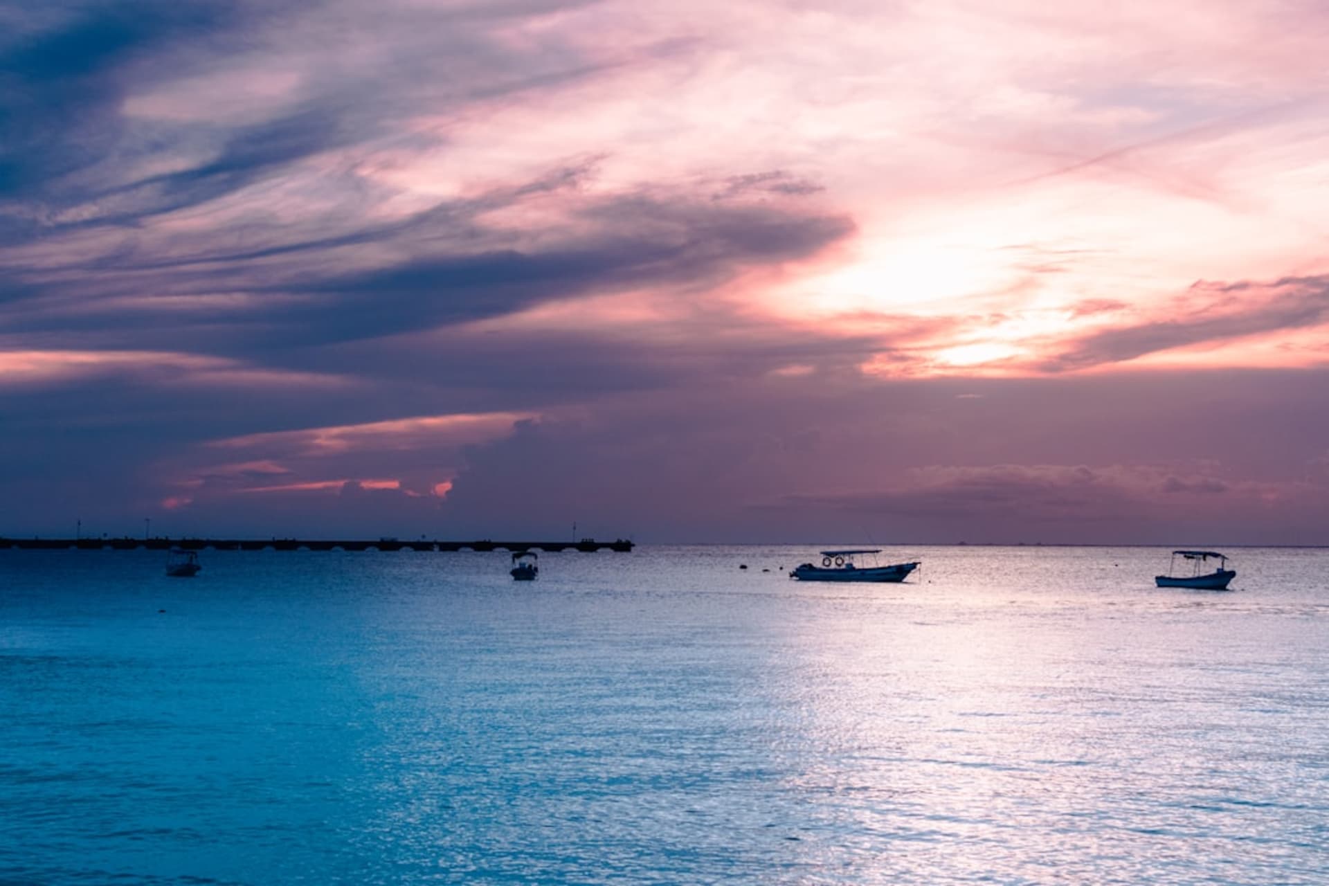 Zihuatanejo's deep natural bay at dusk, fishing boats moored in the calm water below the town's hillside houses, the Pacific horizon beyond the bay entrance, the sky turning orange and purple