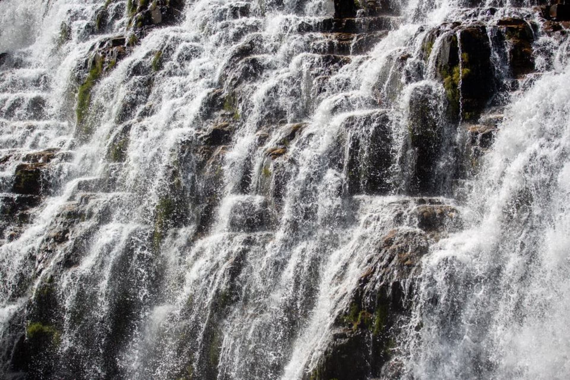 Wide curtain of water cascading over a rock ledge into a jungle pool at Kepirohi Waterfall, Pohnpei