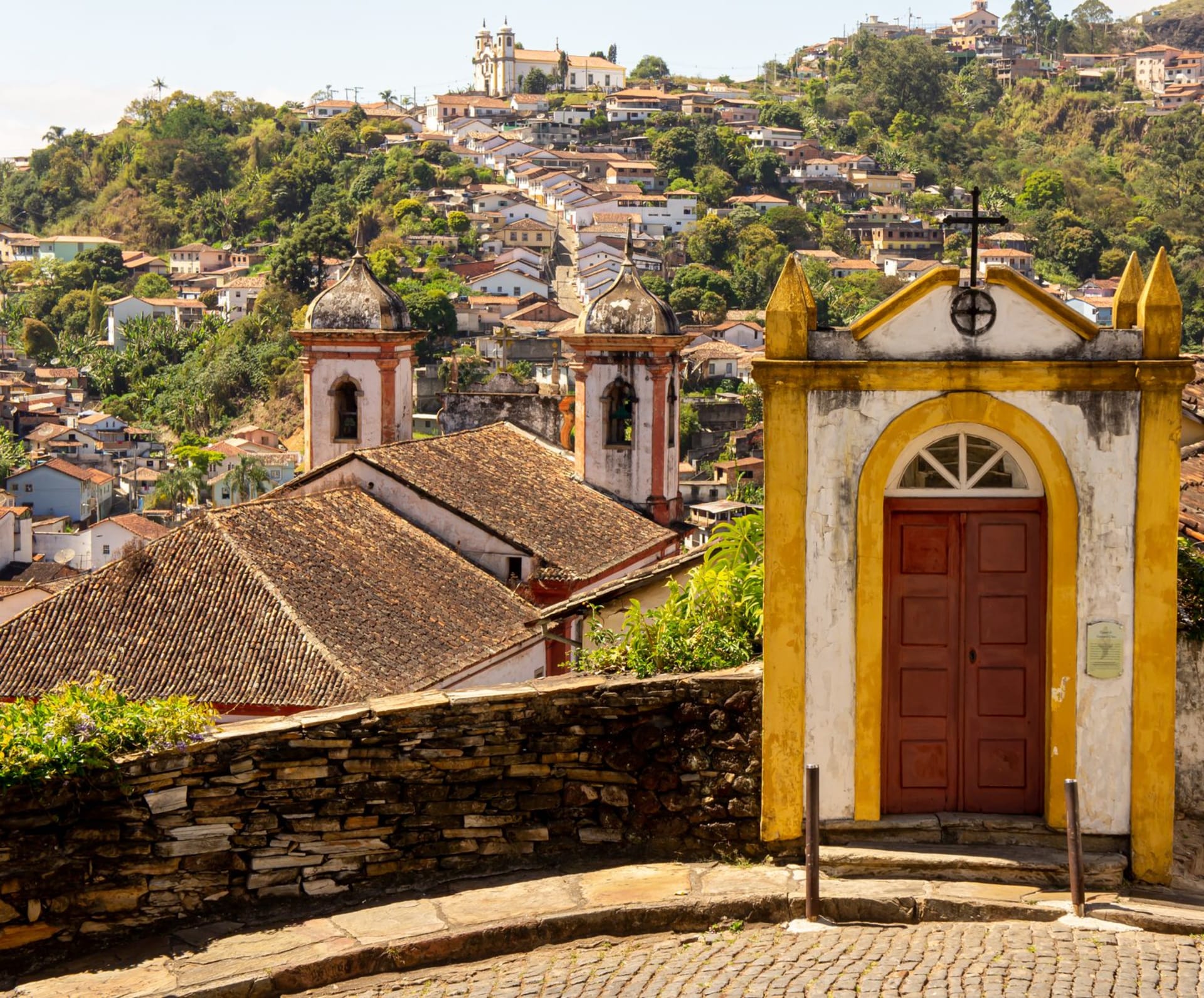 Ornate colonial church facade in Ouro Preto, Minas Gerais, with whitewashed walls and gilded towers rising against a blue sky