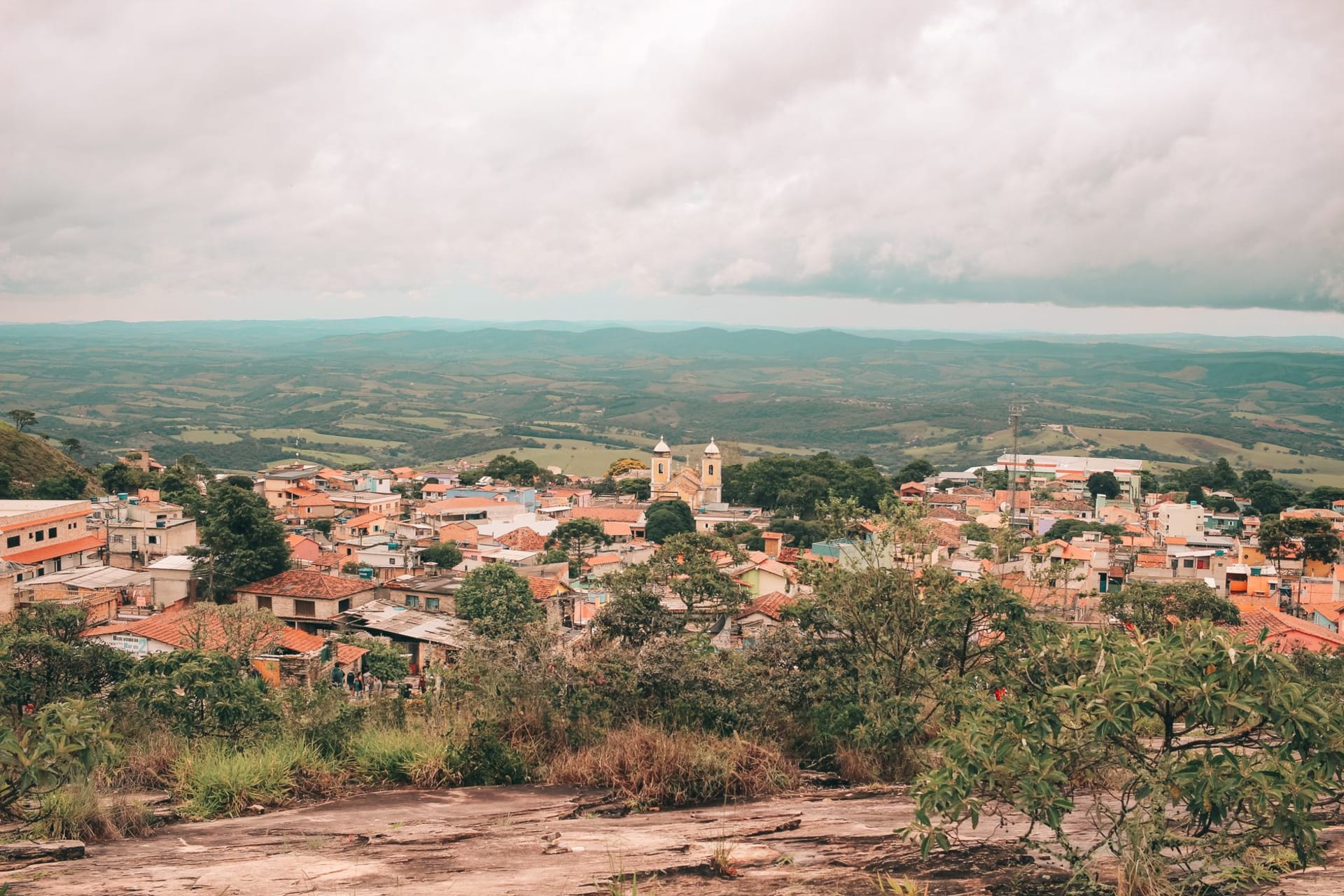 A misty morning view of Serro's colonial church towers and red-tiled rooftops rising from the green mountain valley in Minas Gerais