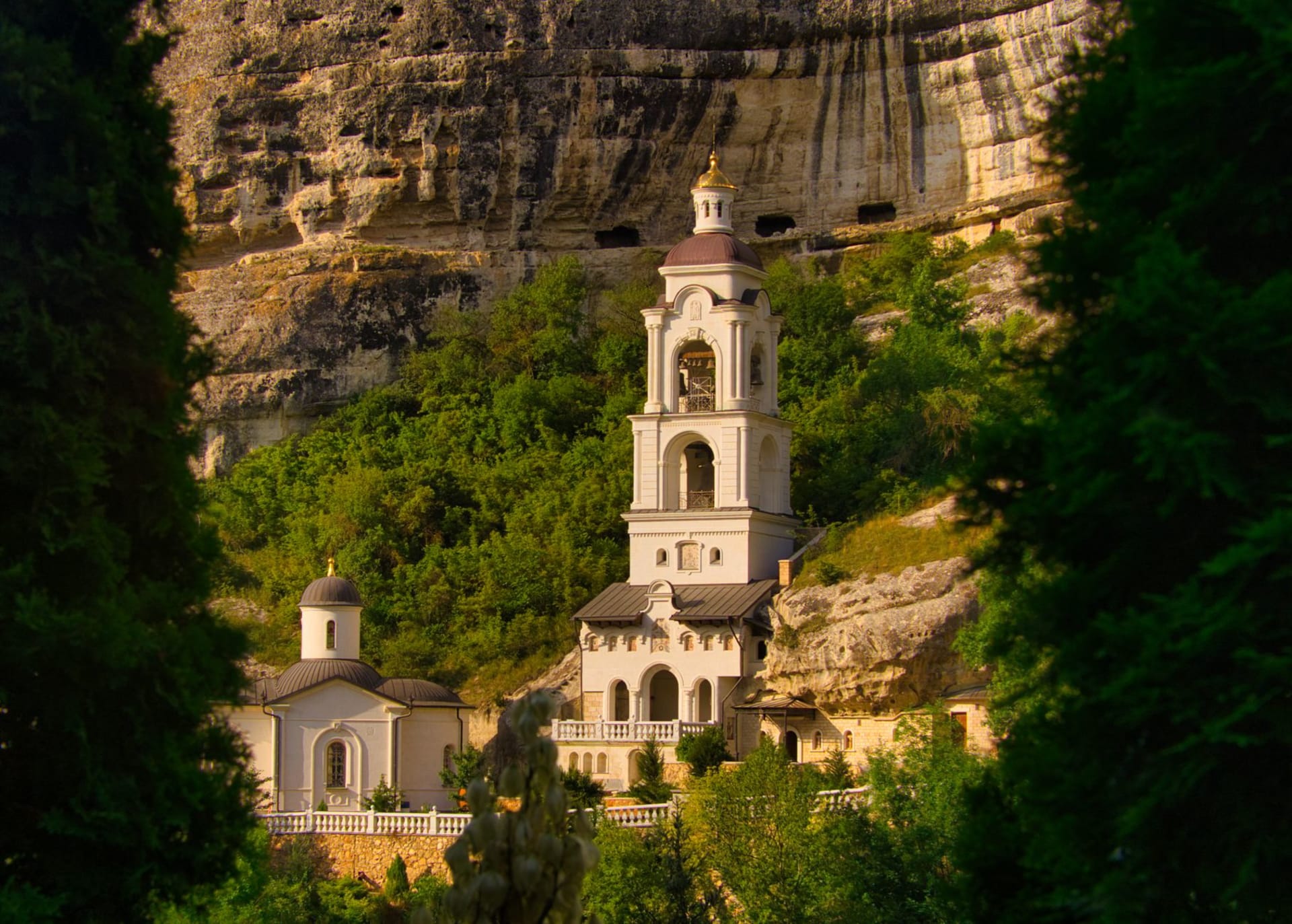 El complejo de la iglesia del Monasterio de Rudi con muros blancos anidado en bosque denso sobre un escarpado acantilado sobre el ancho río Dniéster en un dramático meandro en herradura, perspectiva aérea