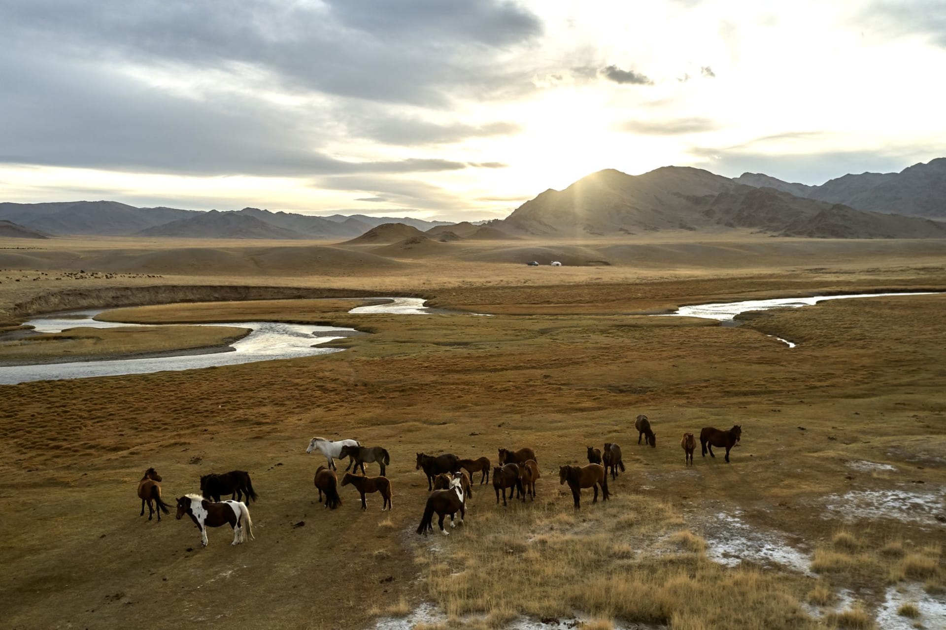 Terkhiin Tsagaan Lake reflecting the sky, with the dark cone of Khorgo volcano visible on the far shore and grass banks in the foreground
