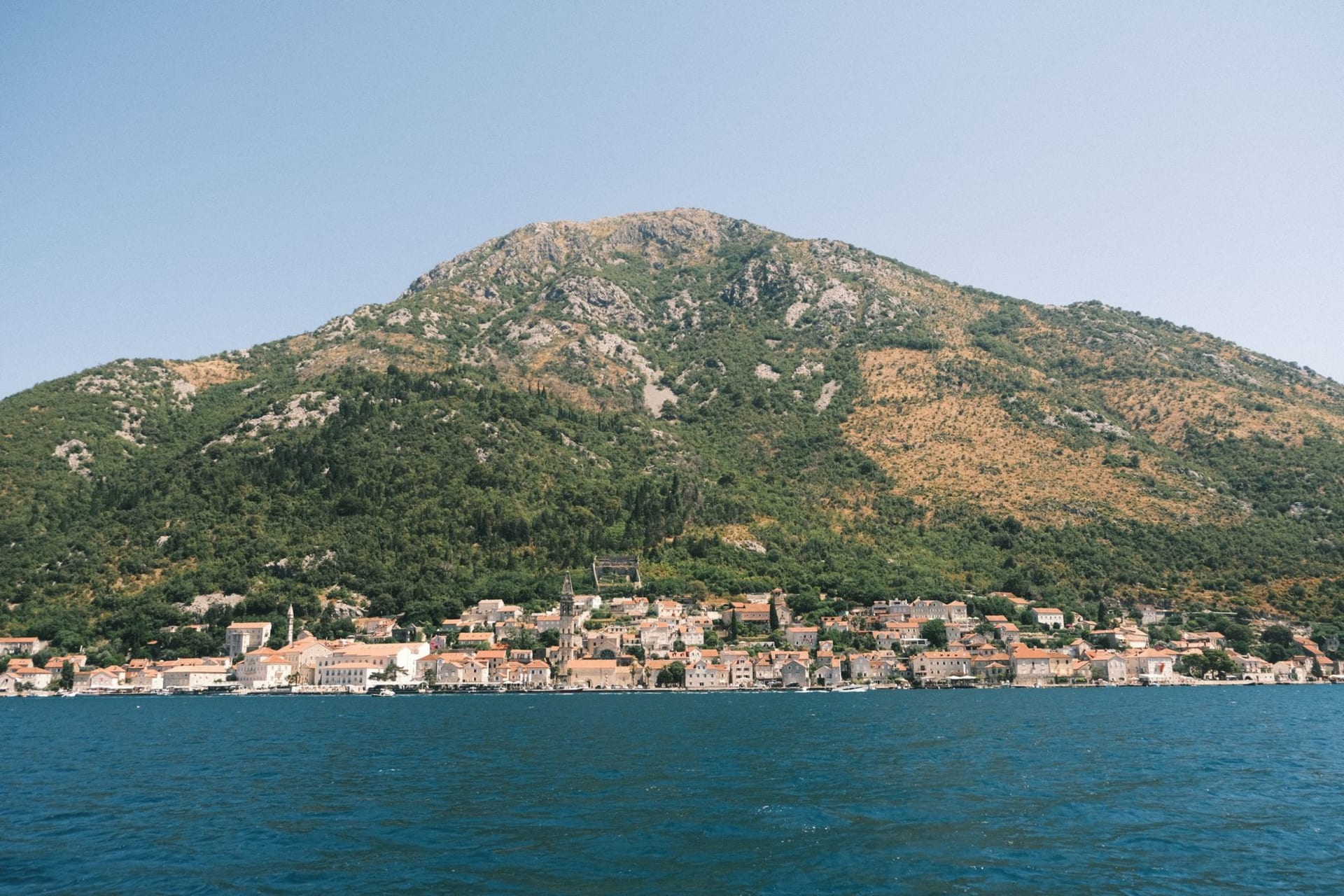 The village of Perast with its baroque bell towers reflected in the mirror-still water of the Bay of Kotor, Our Lady of the Rocks island in the background