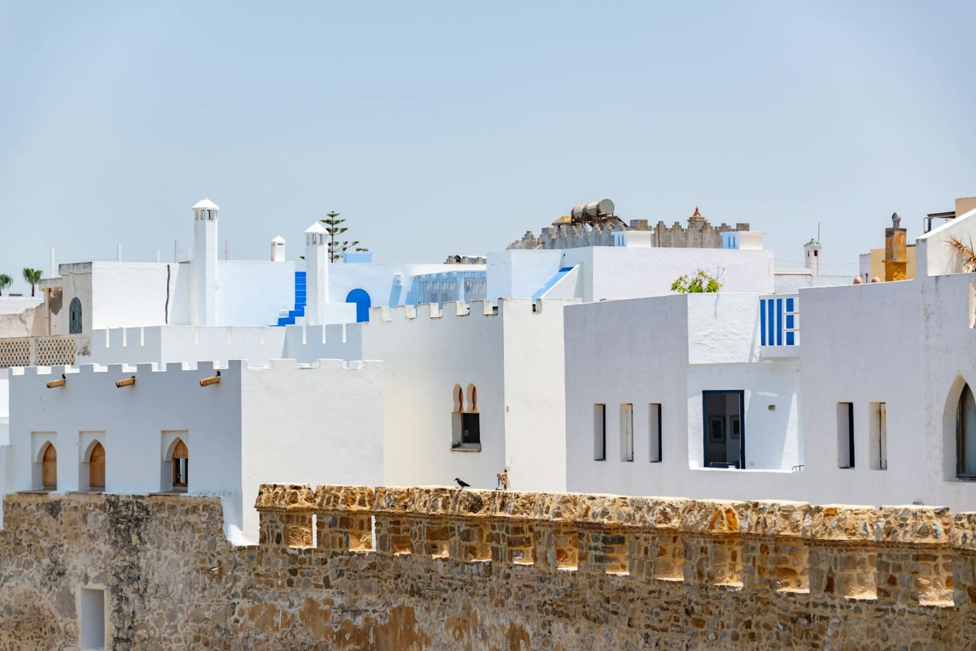 Whitewashed walls of Asilah's medina painted with vivid murals, the Atlantic visible beyond the Portuguese ramparts in late afternoon light.