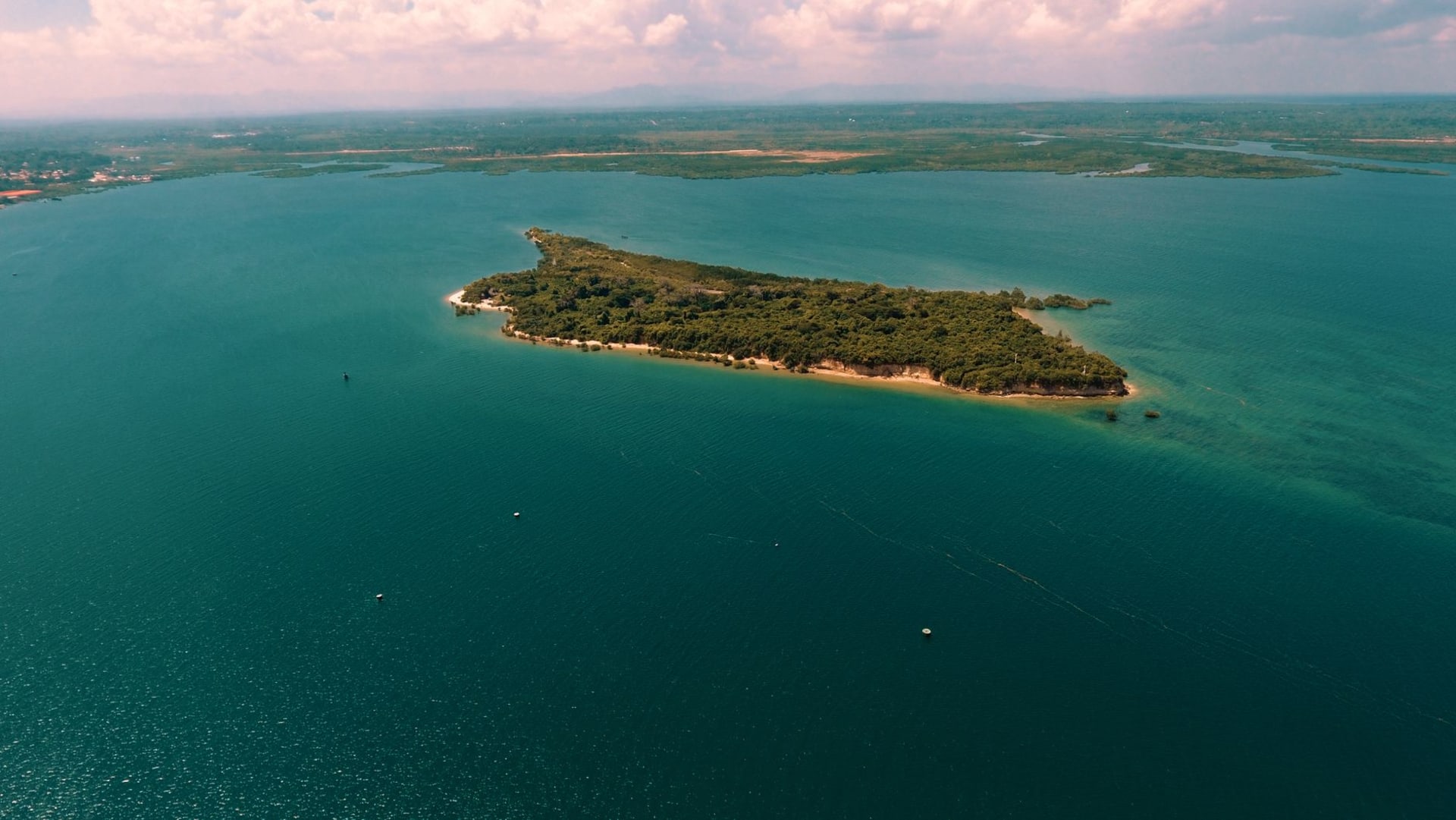 Aerial view of a Quirimbas coral island ringed by turquoise reef with traditional dhow sailing through clear water