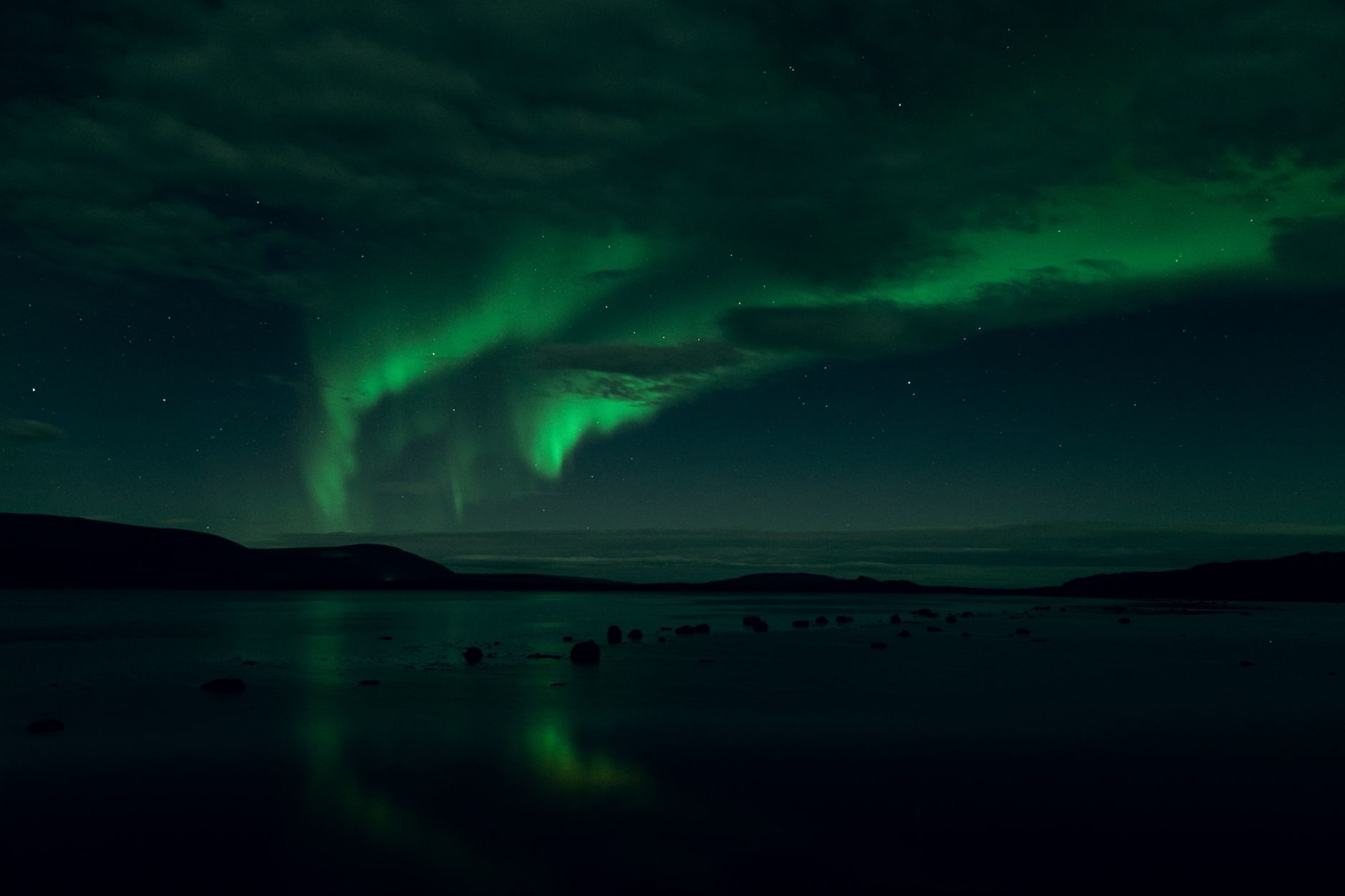 Green aurora borealis sweeping across a dark Arctic sky above a snow-covered landscape