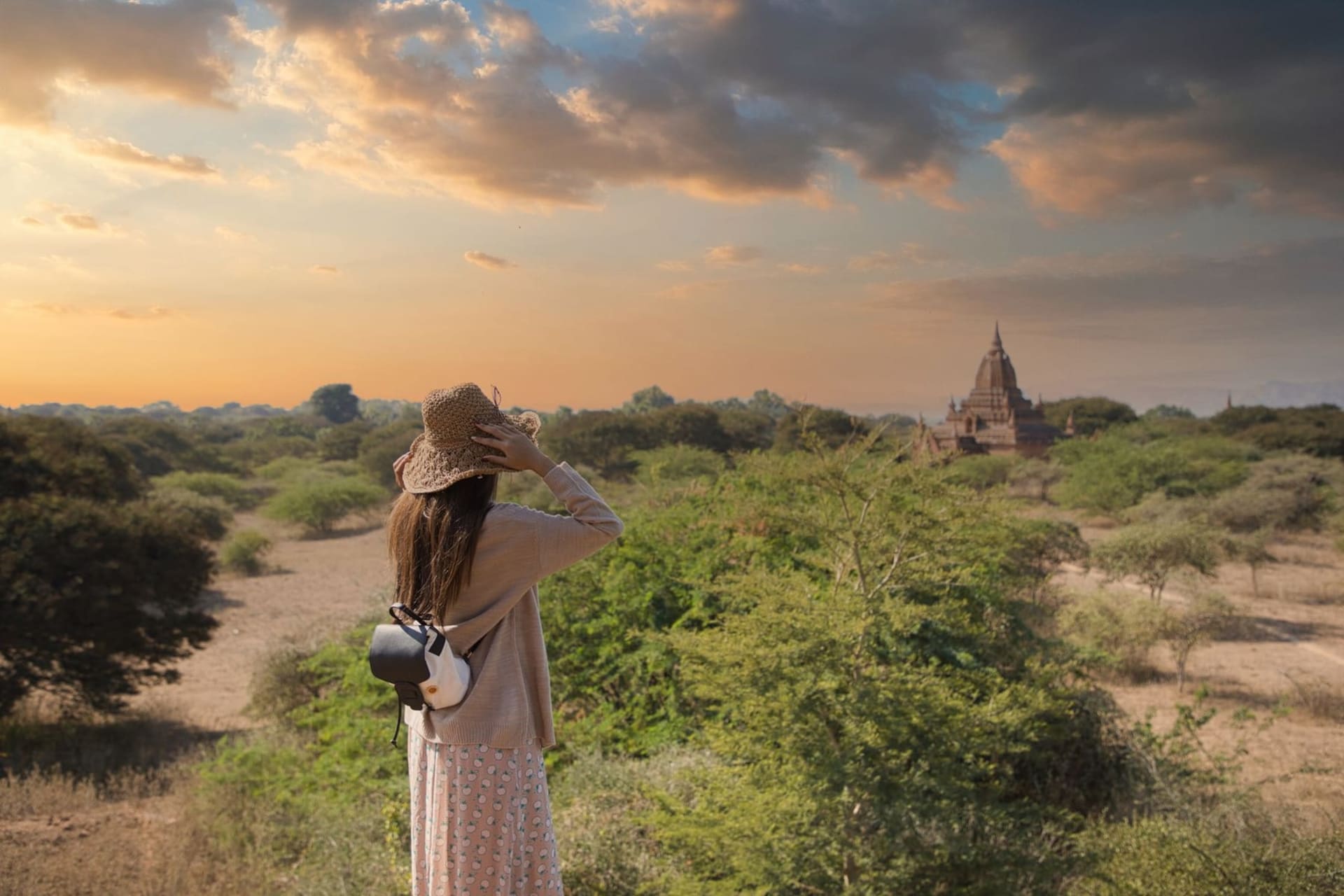Dozens of ancient red-brick Buddhist pagodas and temples rising from a flat, misty plain at sunrise, with a hot-air balloon drifting silently above them against a pale amber sky.