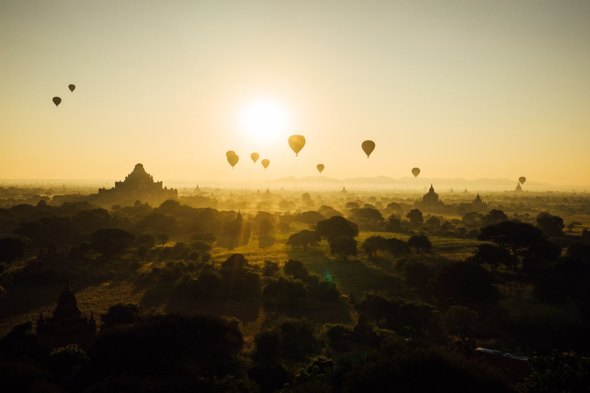 Hot air balloons floating over the ancient pagodas of Bagan at sunrise, silhouetted against a golden sky