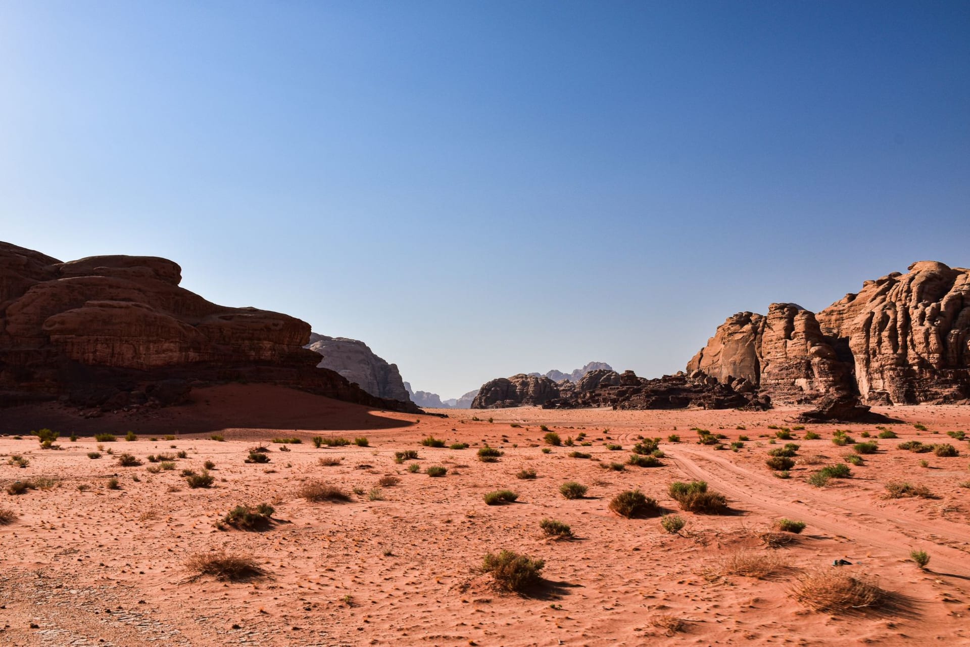 Enormous sandstone monoliths rising from a sea of red sand in Wadi Rum at sunset, the sky turning deep orange