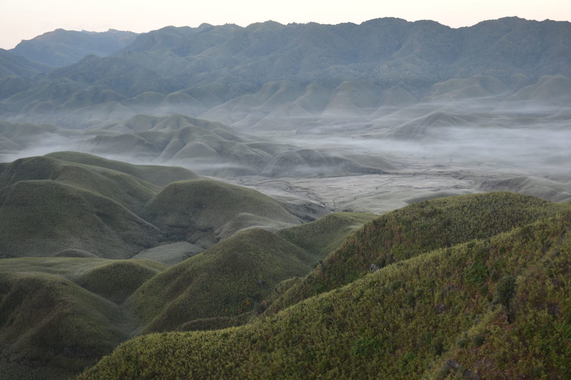 Cluster of thatched Konyak longhouses on a misty forested ridge at Longwa, blue mountains receding toward the Myanmar border