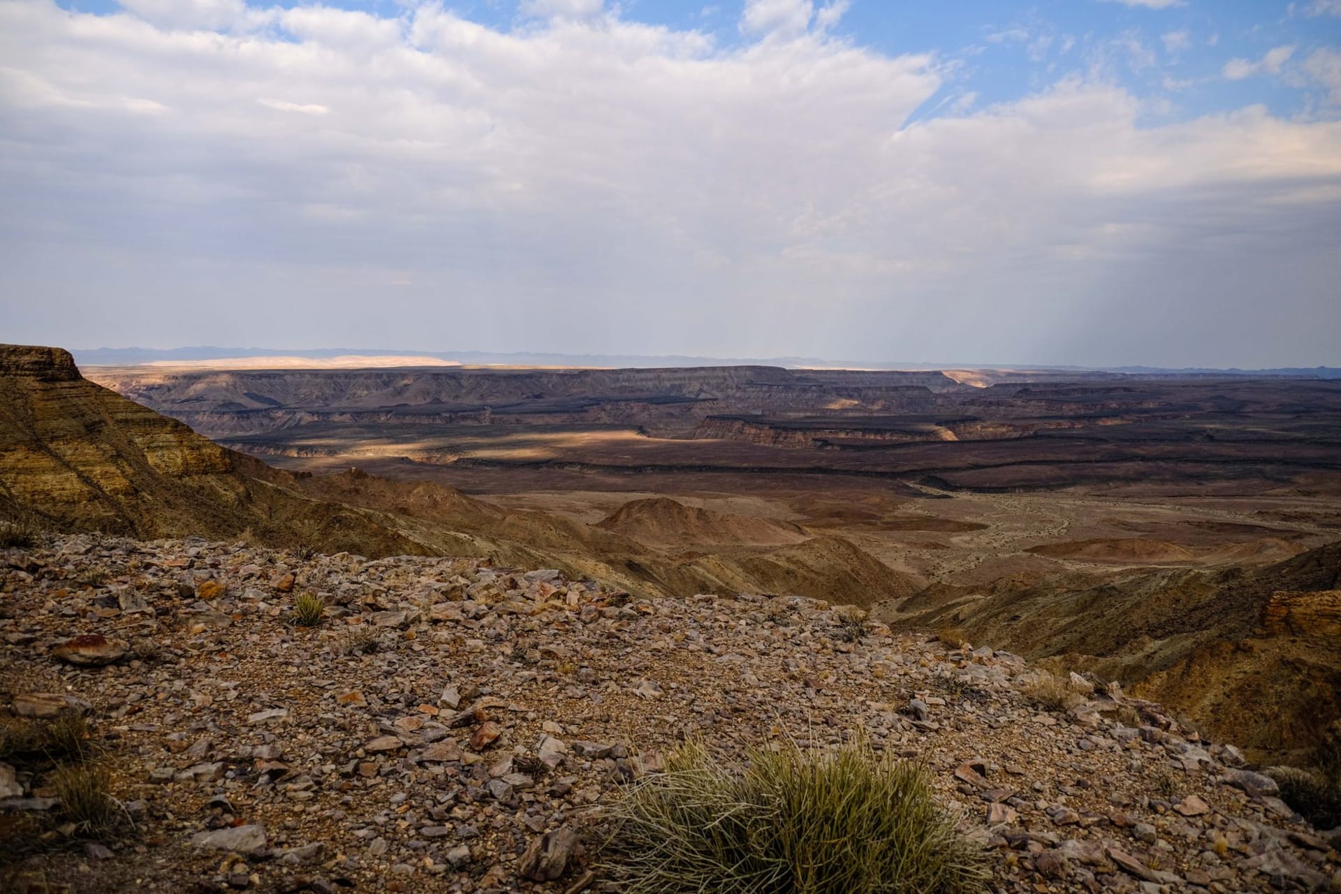 Panoramic view of the Fish River Canyon at golden hour, the winding dry riverbed cutting through layered orange and brown rock below sheer cliffs