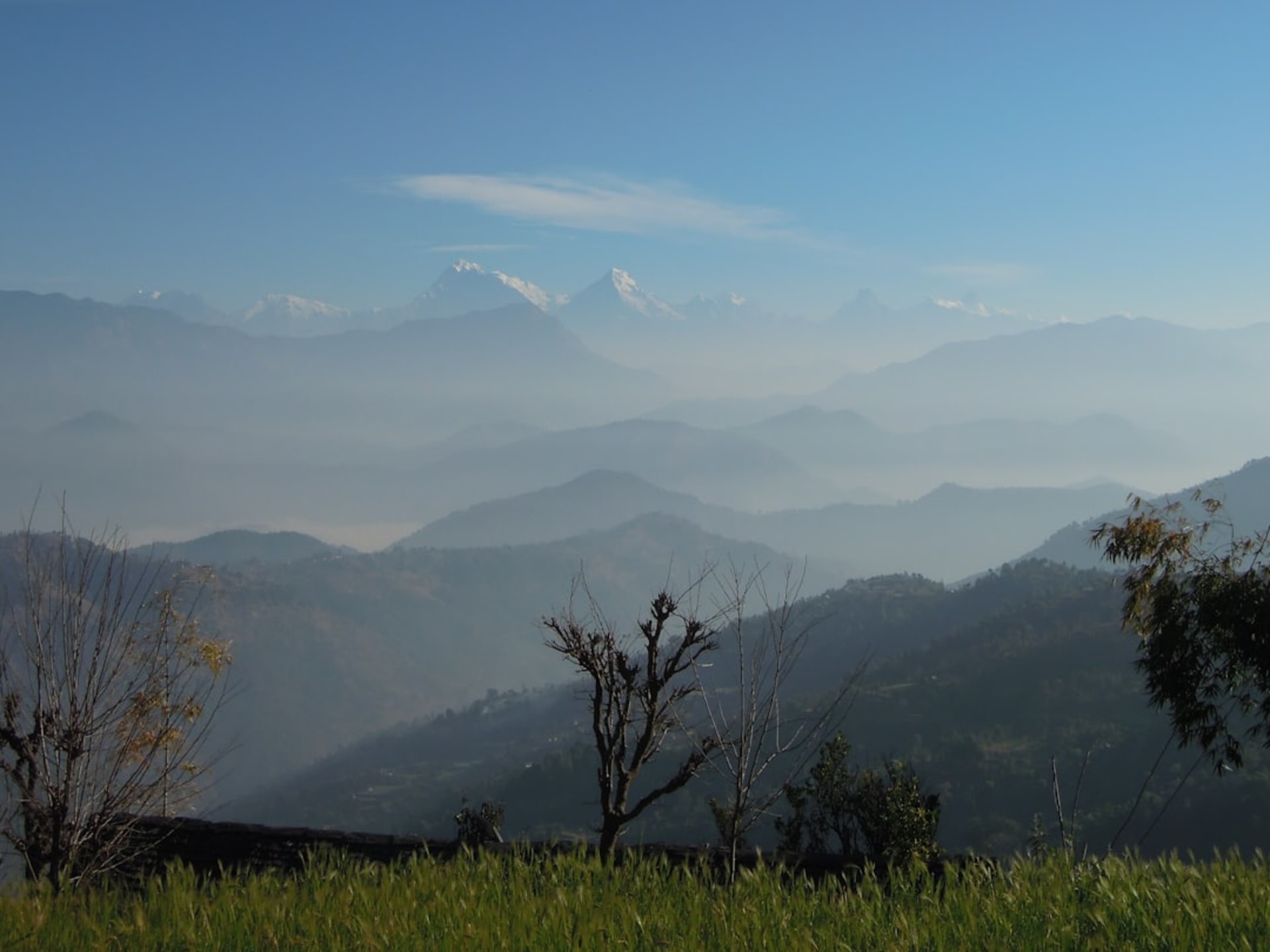 Panorama de la chaîne himalayenne vu depuis la crête de Chisapani à l'aube, avec une prairie au premier plan et des silhouettes de montagnes étagées