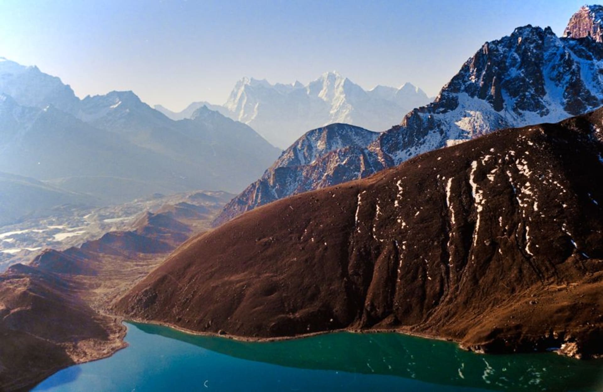 Les eaux turquoise du lac Dudh Pokhari au village de Gokyo, ceinturé de moraine grise avec des sommets enneigés se reflétant sur la surface immobile