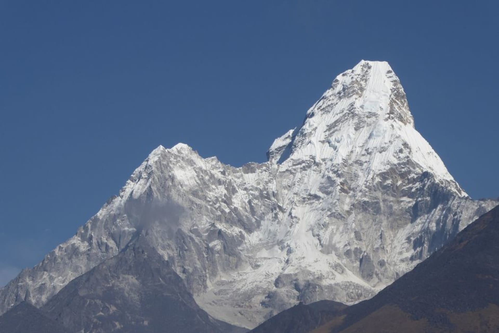 Exterior courtyard of the International Mountain Museum in Pokhara with a replica stone Sherpa house and mountain-shaped architecture against a blue sky