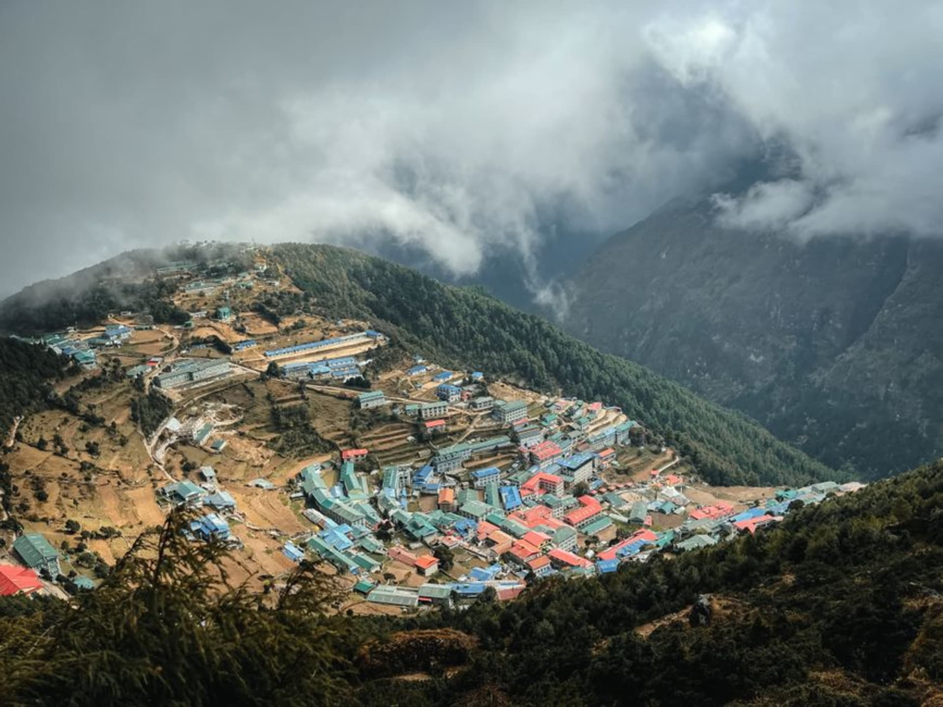 Casas de piedra en terraza de Namche Bazaar elevándose en un anfiteatro en forma de herradura contra laderas montañosas empinadas y verdes, con banderas de oración tendidas sobre los tejados
