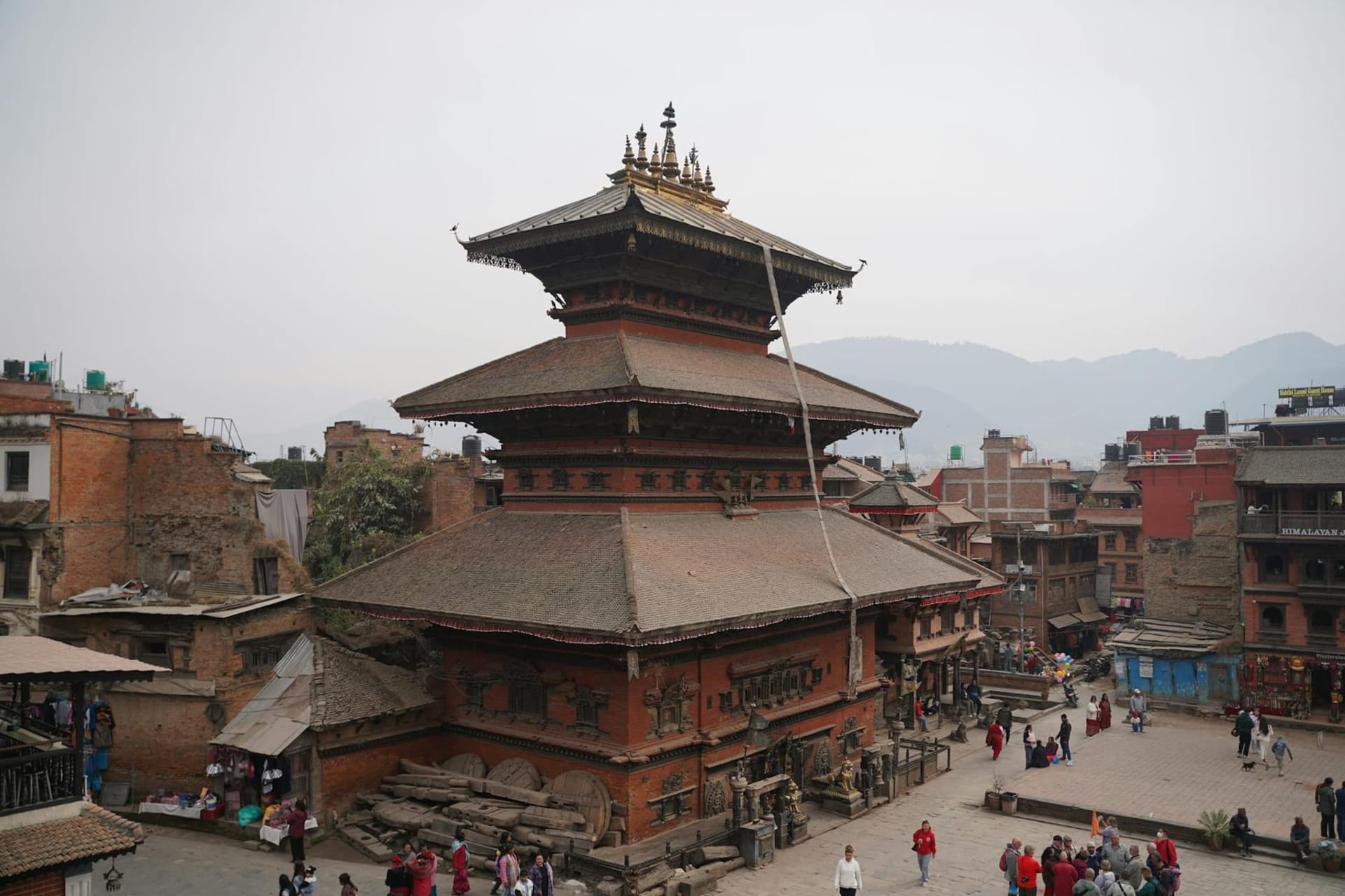 Tiered pagoda temples rising above Patan's Durbar Square, their carved wooden struts and gilded rooftops glowing amber in morning light against a pale Himalayan sky.