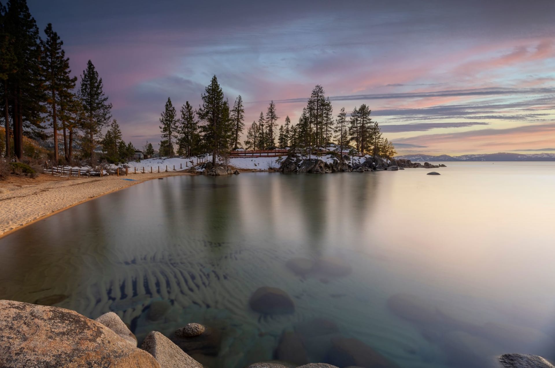 Lake Tahoe's Nevada shore at sunset, the water an impossible cobalt blue, granite boulders in the shallows and the Sierra Nevada rising steeply behind