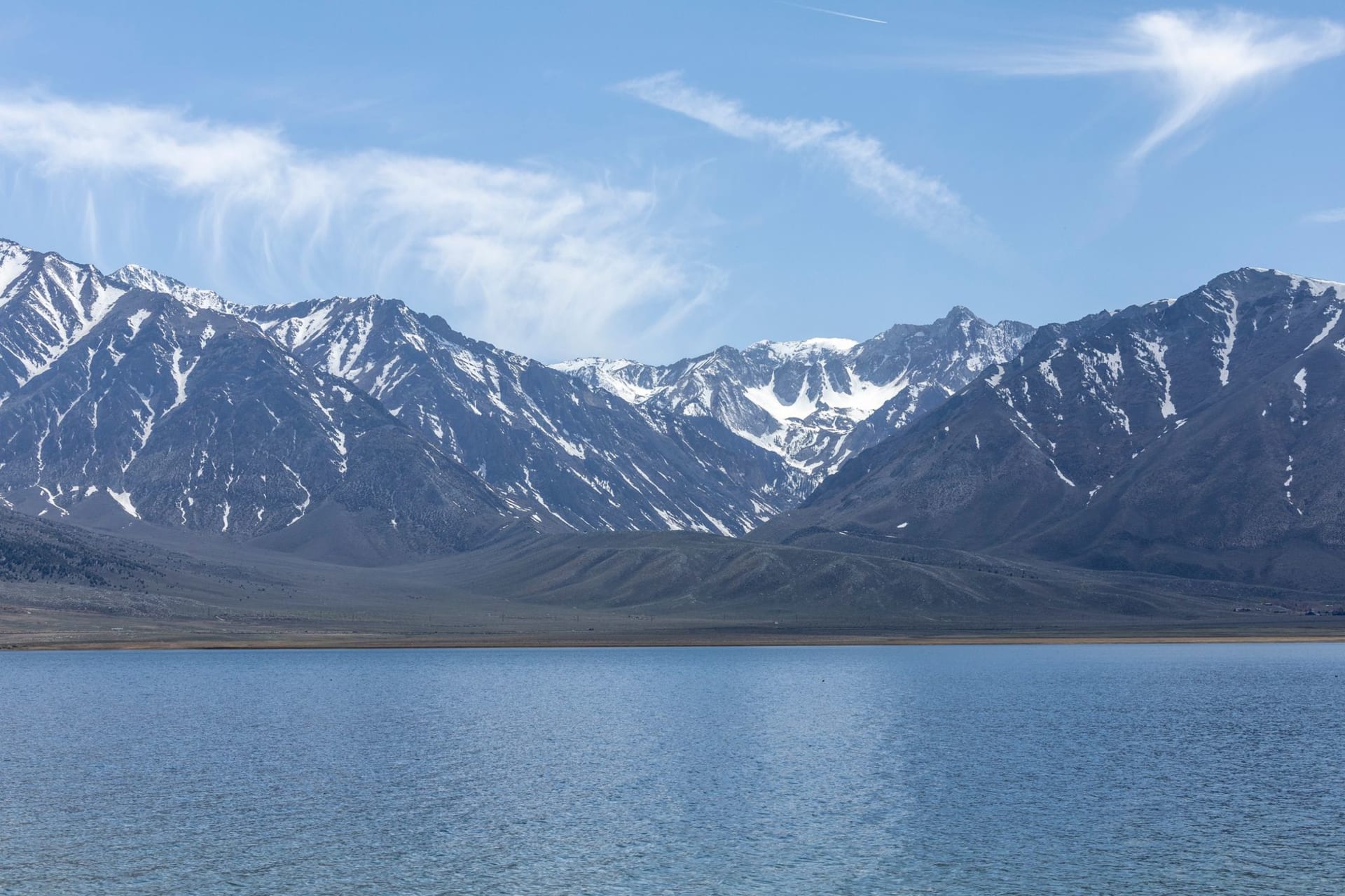 Glacially carved Ruby Mountains peaks rising dramatically above a high alpine lake, the granite ridgeline reflected in still turquoise water