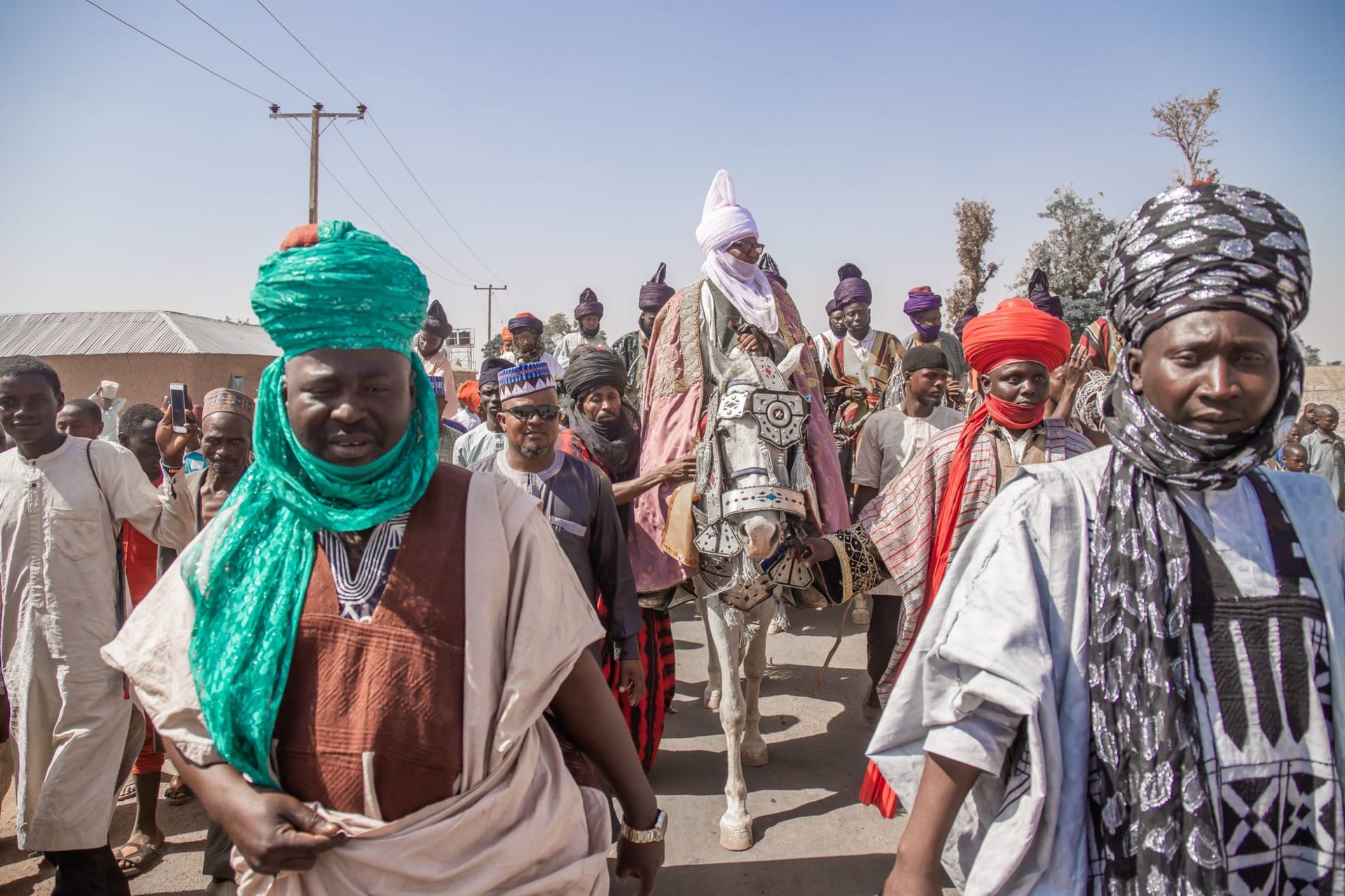 A Tahoua weekly market scene — women in vivid robes selling silver jewelry and calabashes under acacia-shade at the edge of the Sahel