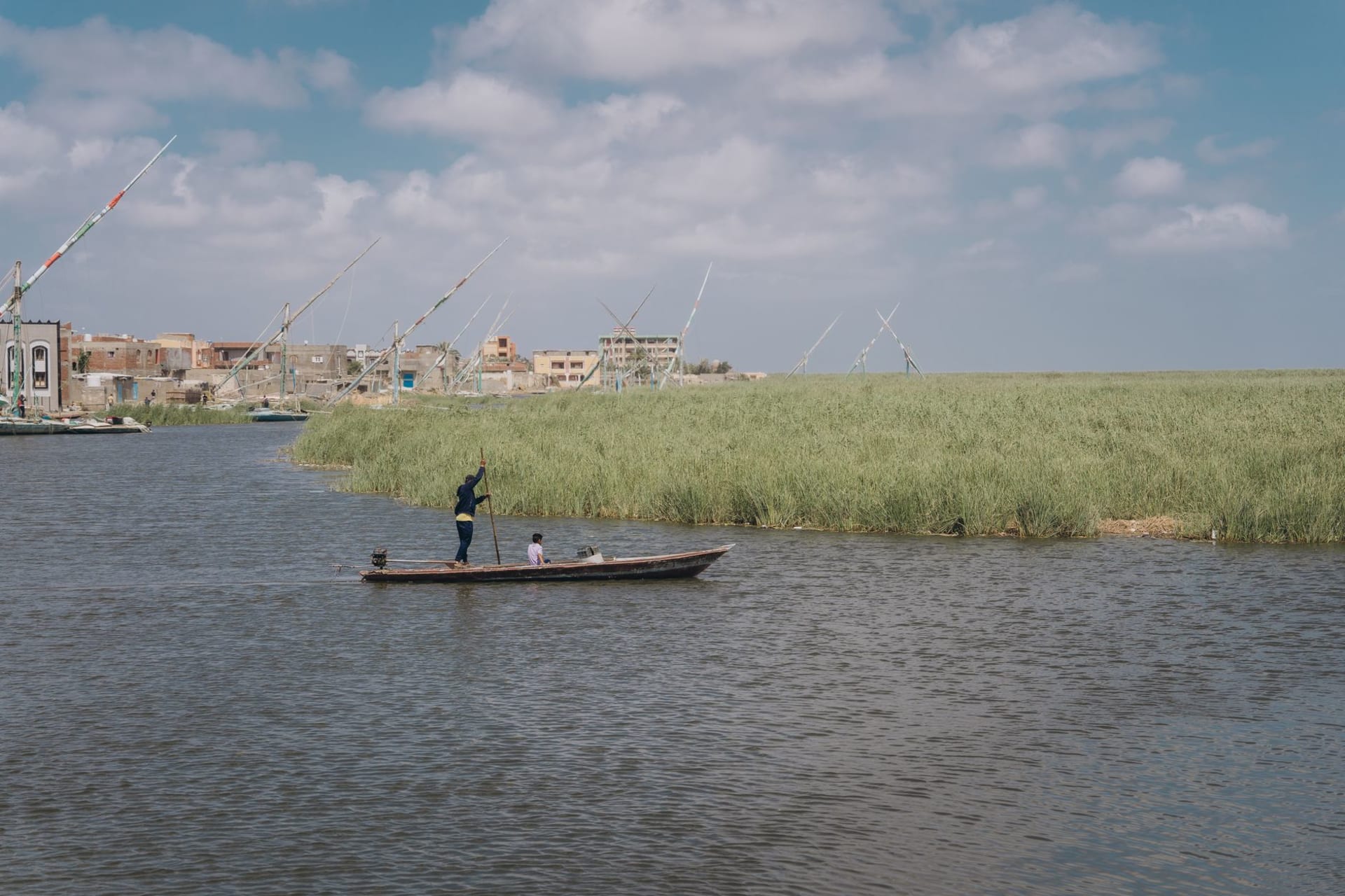 The wide Damietta branch of the Nile at Mansoura at twilight, with city lights beginning to appear on both banks and a felucca crossing midstream