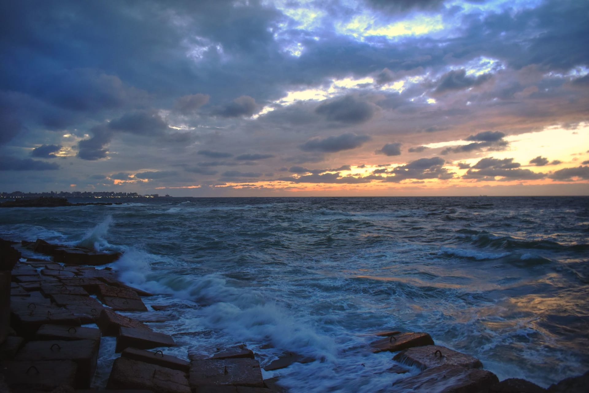 Fiery sunset over the Mediterranean Sea in Alexandria, Egypt, with dramatic clouds reflected in the churning waves