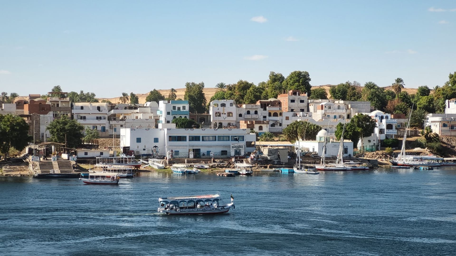 Pink and turquoise Nubian houses on Elephantine Island viewed from Aswan's East Bank, granite boulders and date palms in the foreground