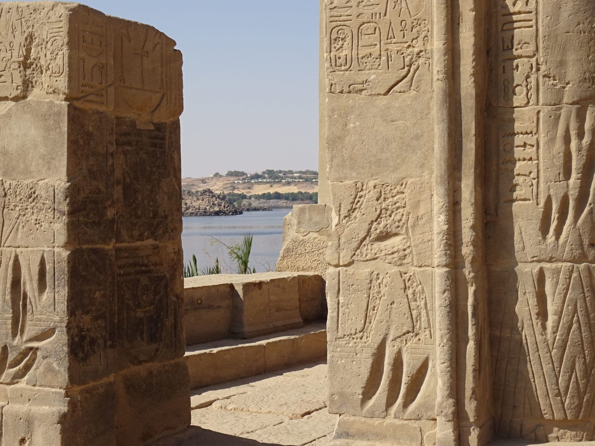 Stone ruins of an ancient Egyptian temple adorned with hieroglyphs beside the Nile River under clear skies