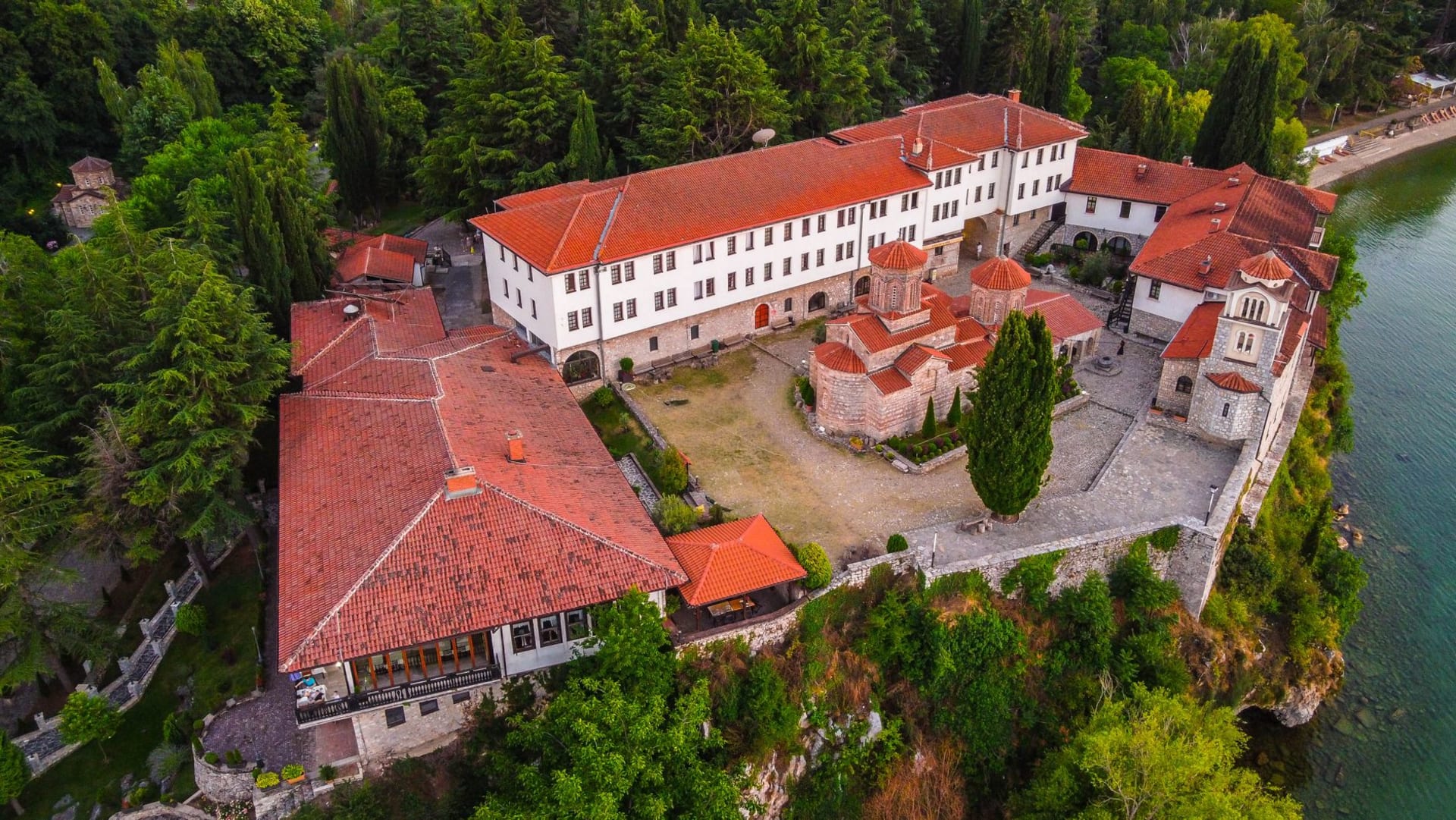 Aerial view of Saint Naum Monastery perched beside the glassy waters of Lake Ohrid, surrounded by dense forest