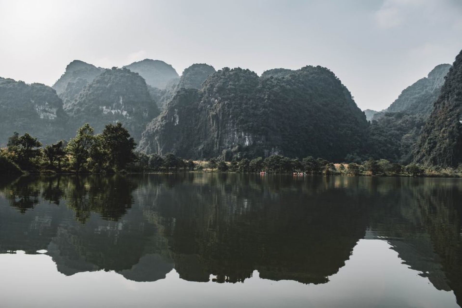 Ba Be Lake at dawn, still water reflecting limestone karst peaks and forested shoreline