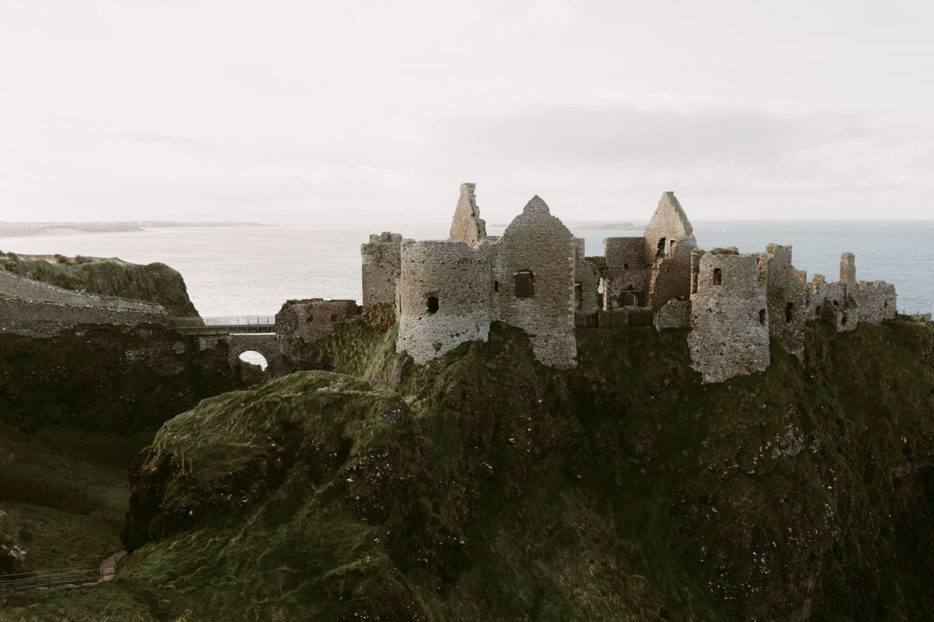 Dunluce Castle ruins perched on a basalt sea stack above the stormy Atlantic, grey sky above and white surf below