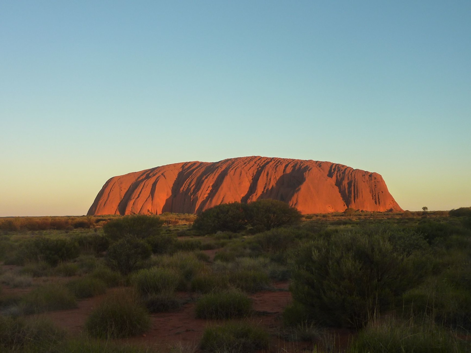 Uluru, the sacred sandstone monolith, glowing deep red and orange under the last light of an Australian outback sunset